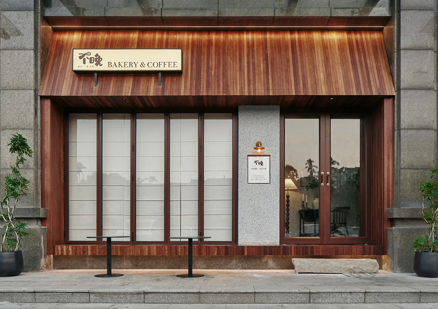 A bakery and coffee shop with a wooden exterior, two dining tables, chairs, and a potted plant, set against a bright background