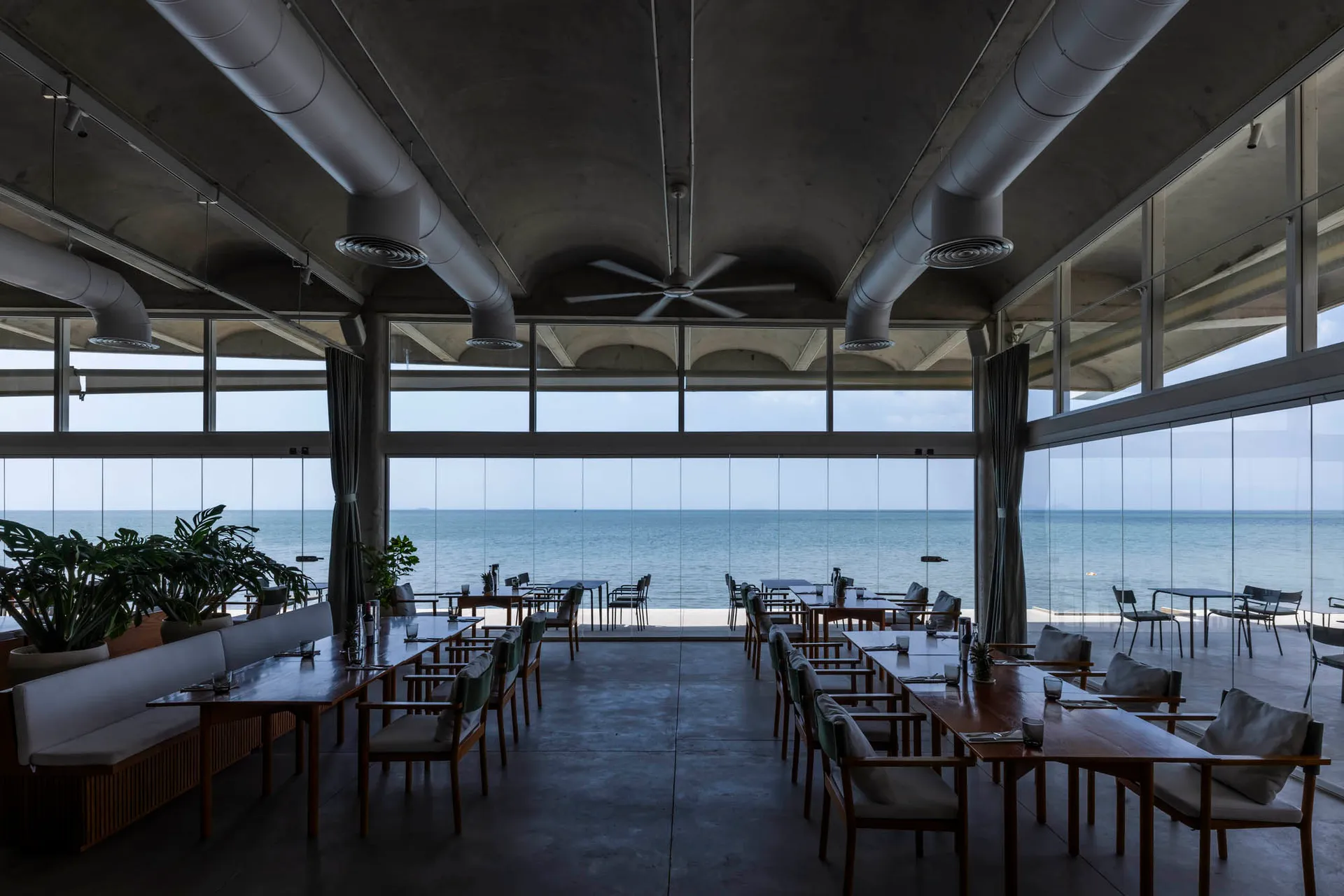 Dining area with multiple tables and chairs, large window overlooking the ocean, and a relaxed atmosphere