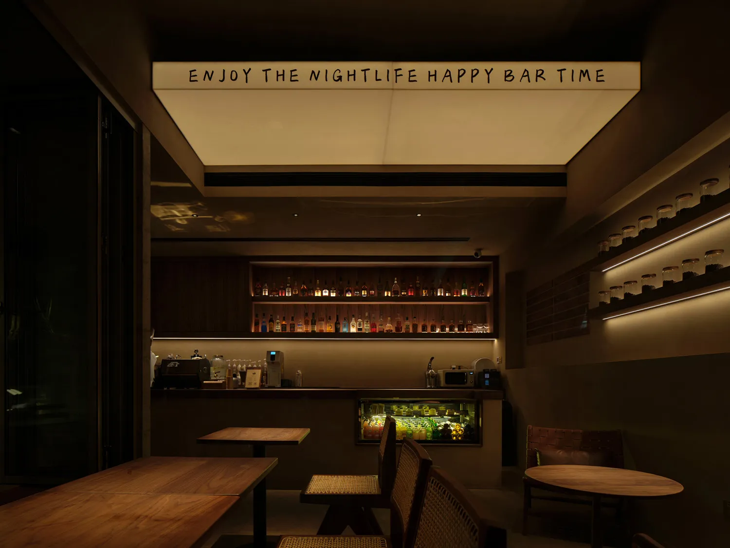 A cozy bar area with wooden tables and chairs, bottles, and a counter, creating a warm and inviting atmosphere