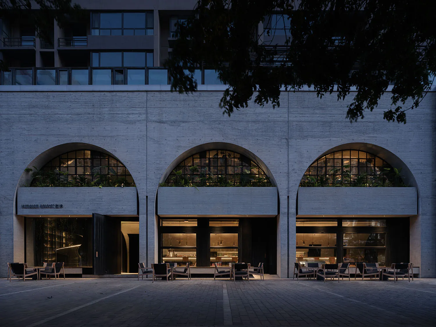 A rendered scene of a building with a stone exterior, featuring multiple arches, chairs, and potted plants, conveying a sophisticated and inviting atmosphere