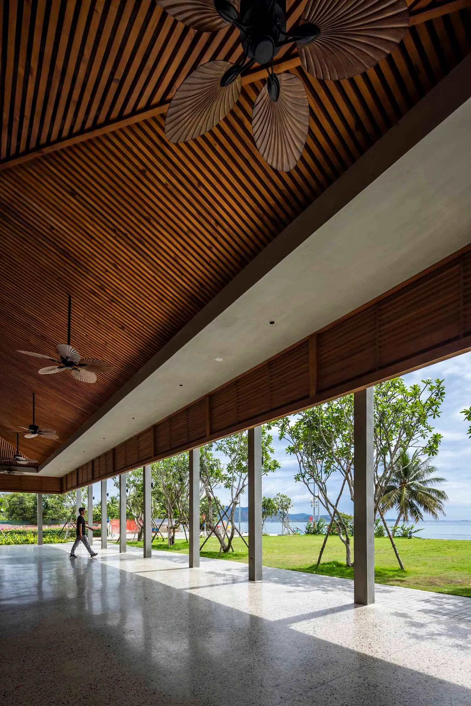 Warm and inviting open-plan space with wooden beams, a large window, and natural light, featuring a living area and dining space with chairs and a person walking through
