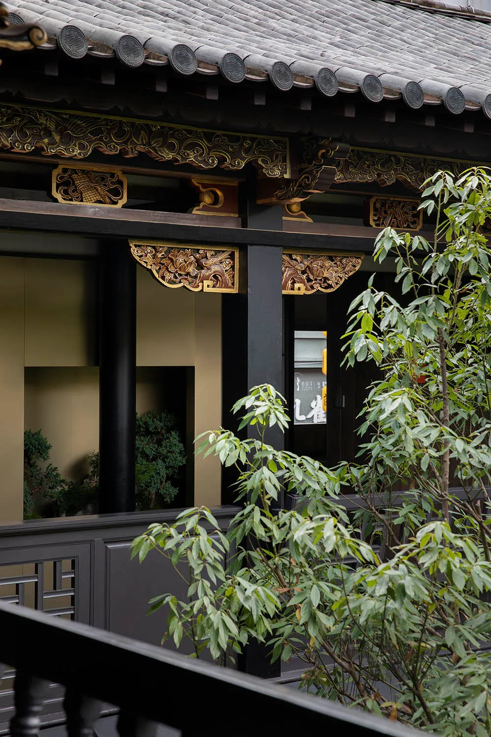 An Asian-style building with a balcony overlooking a garden area, featuring black pillars and gold accents, with potted plants adding to the serene ambiance