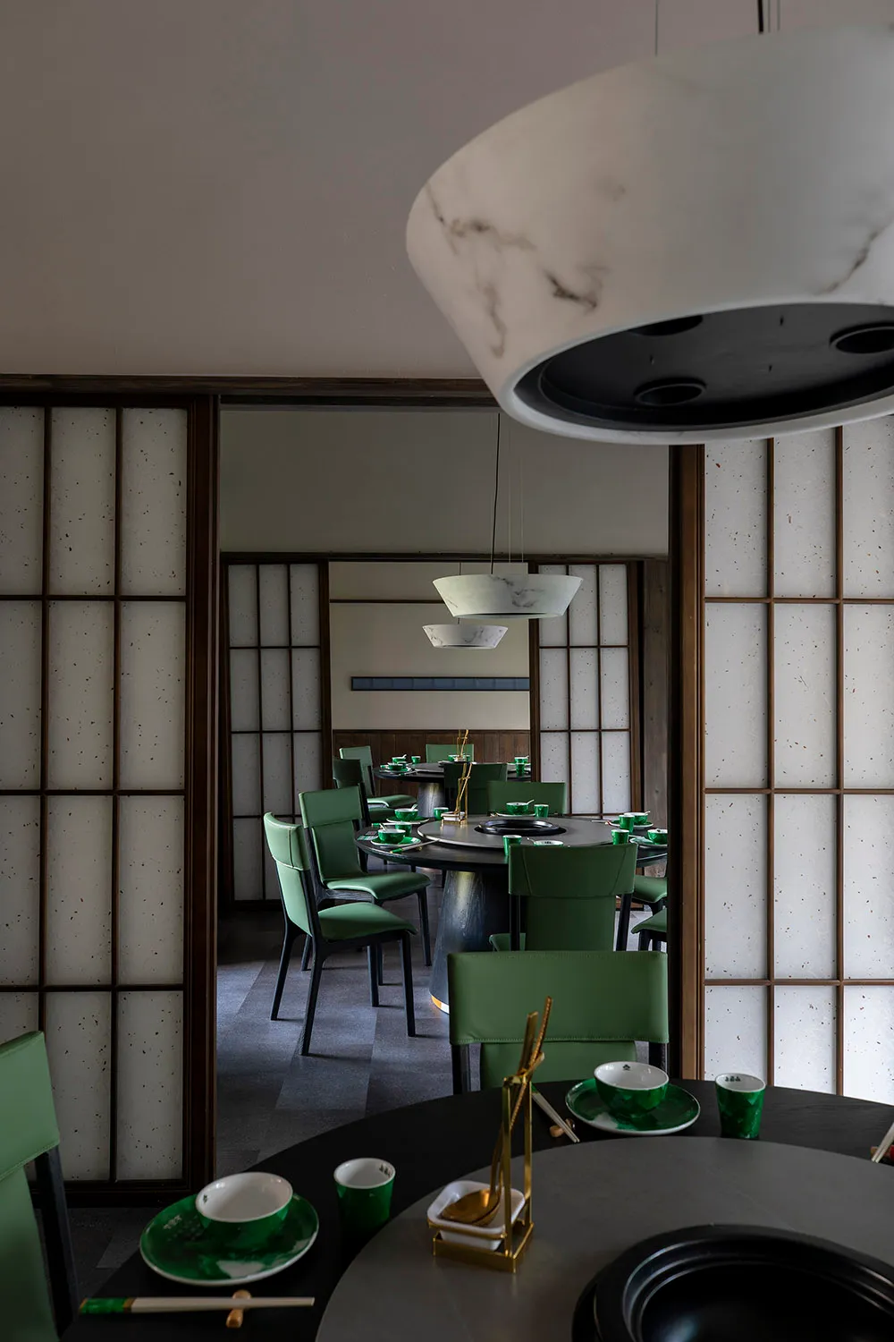A modern restaurant interior with Asian-inspired decorations, dark wood flooring, and dim lighting, featuring tables, chairs, and tableware