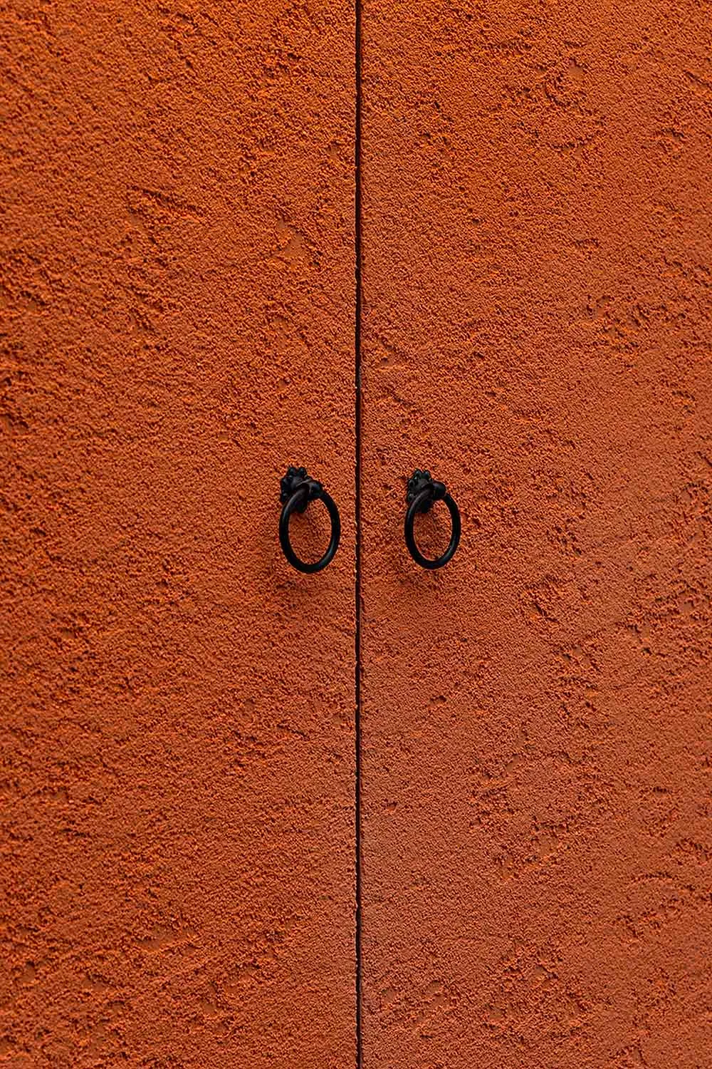 A simple doorway with an orange wall and two black door handles or hinges