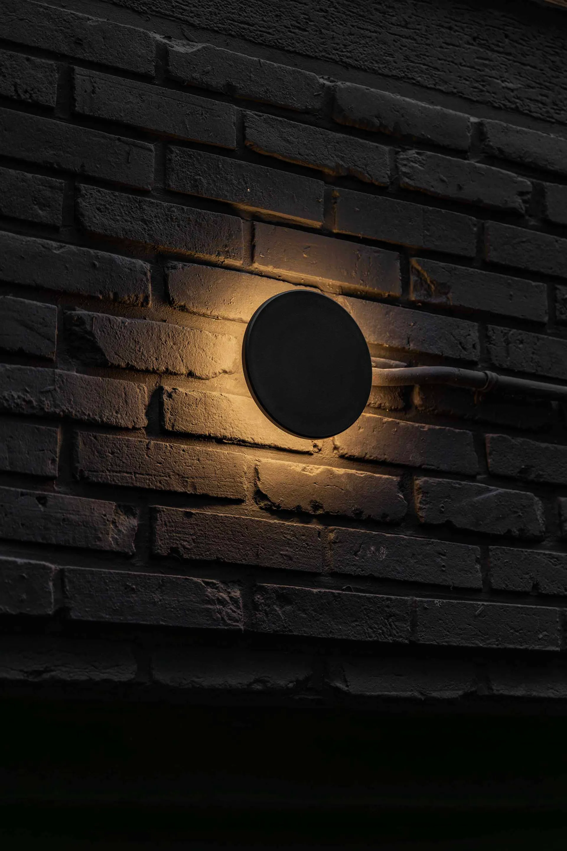 A brick wall with a round light fixture mounted on it, creating a warm atmosphere with the brick adding rustic charm