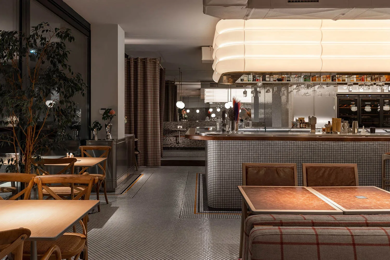 A restaurant interior with a bar area and tables, featuring bottles and comfortable seating for socializing and dining