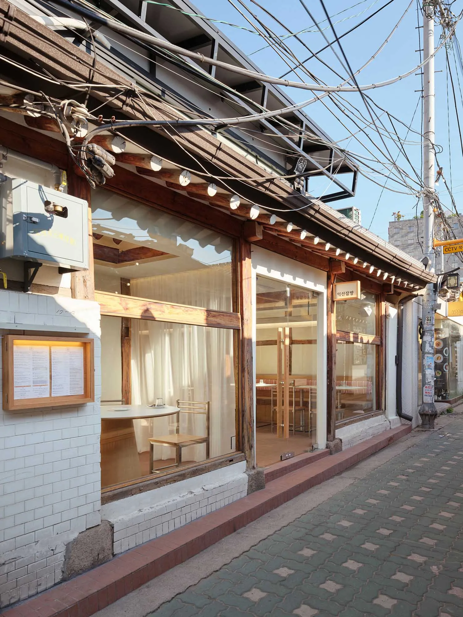 光線充足的木質內裝餐廳用餐區，設有多張桌椅、窗戶自然光線，以及白色桌巾