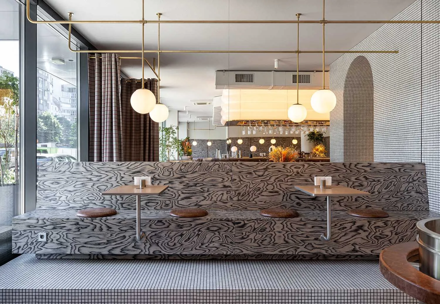 Modern restaurant interior with a bar, dining table, chairs, and unique patterned walls, accented with bottles and ambient lighting