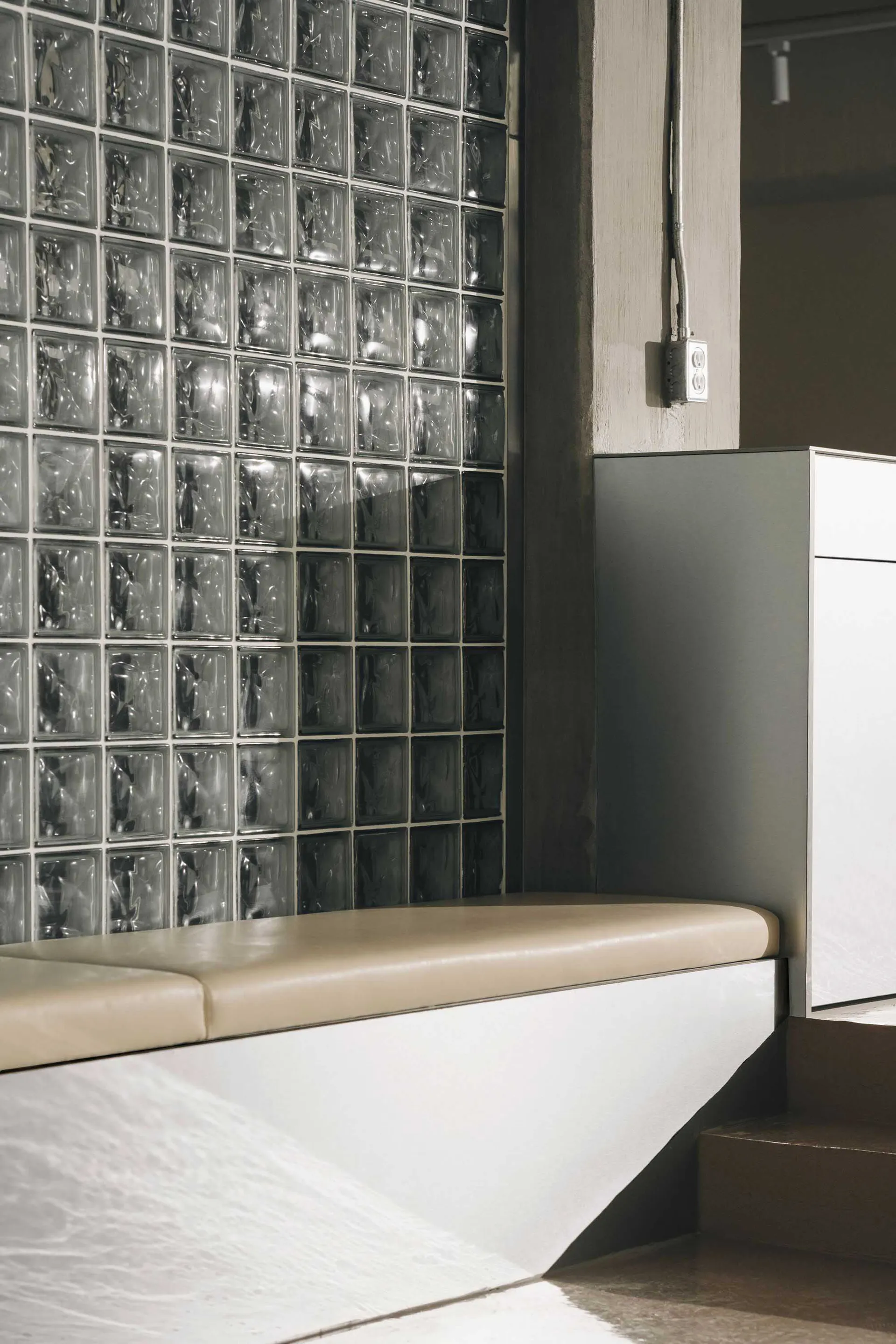 A modern interior design featuring a glass and wood bench in front of a glass block wall, creating a calm and inviting atmosphere with a sense of openness