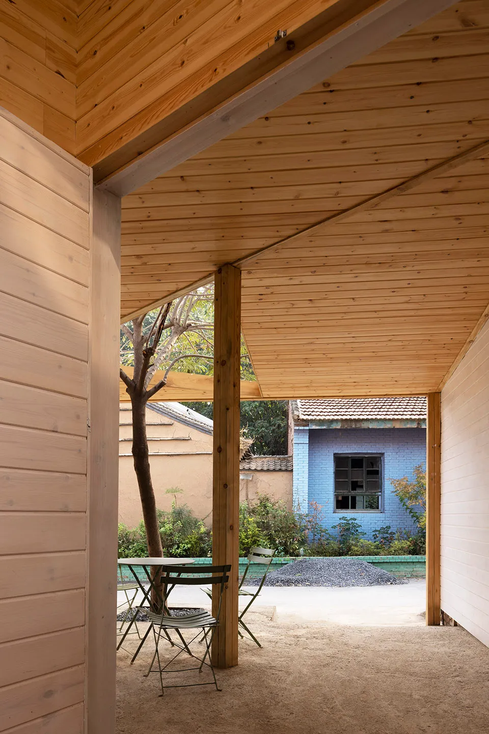 A calm and inviting outdoor patio with wooden walls, a green table, and two chairs, set in front of a blue building