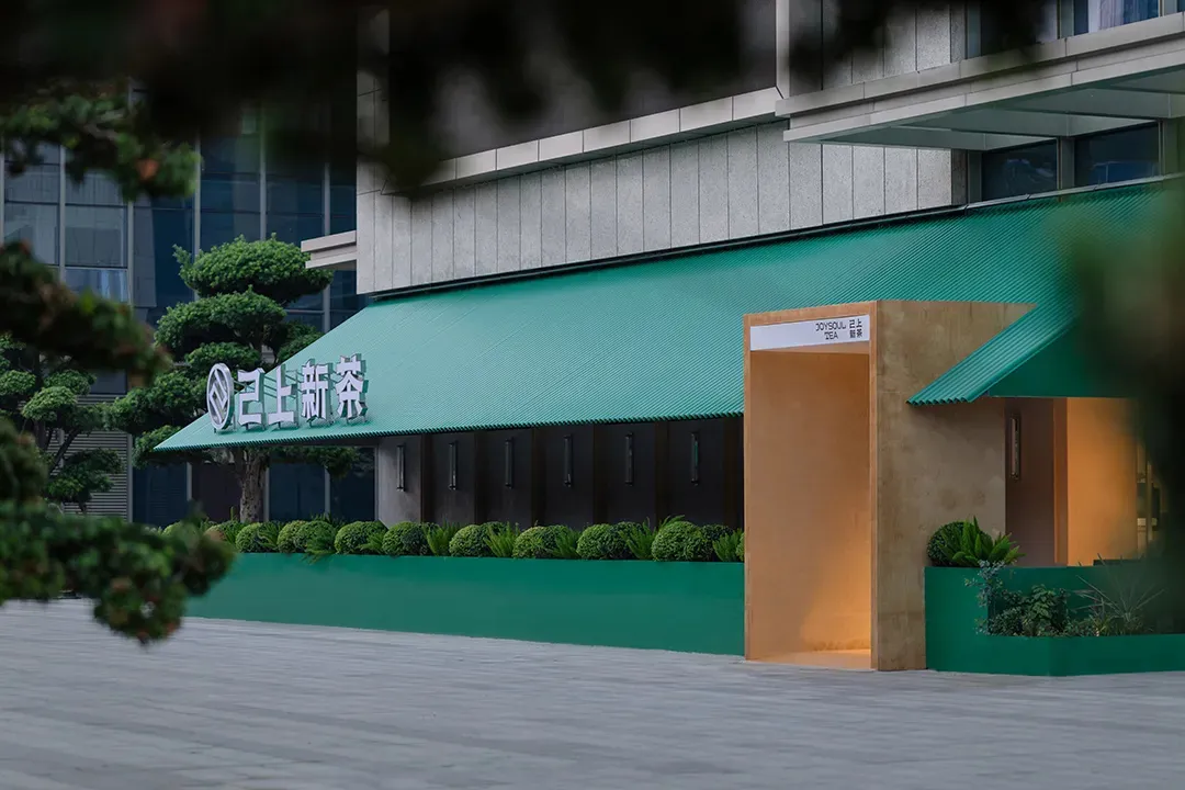 A restaurant with a mix of modern and traditional architecture, featuring green awnings, potted plants, and a dining table