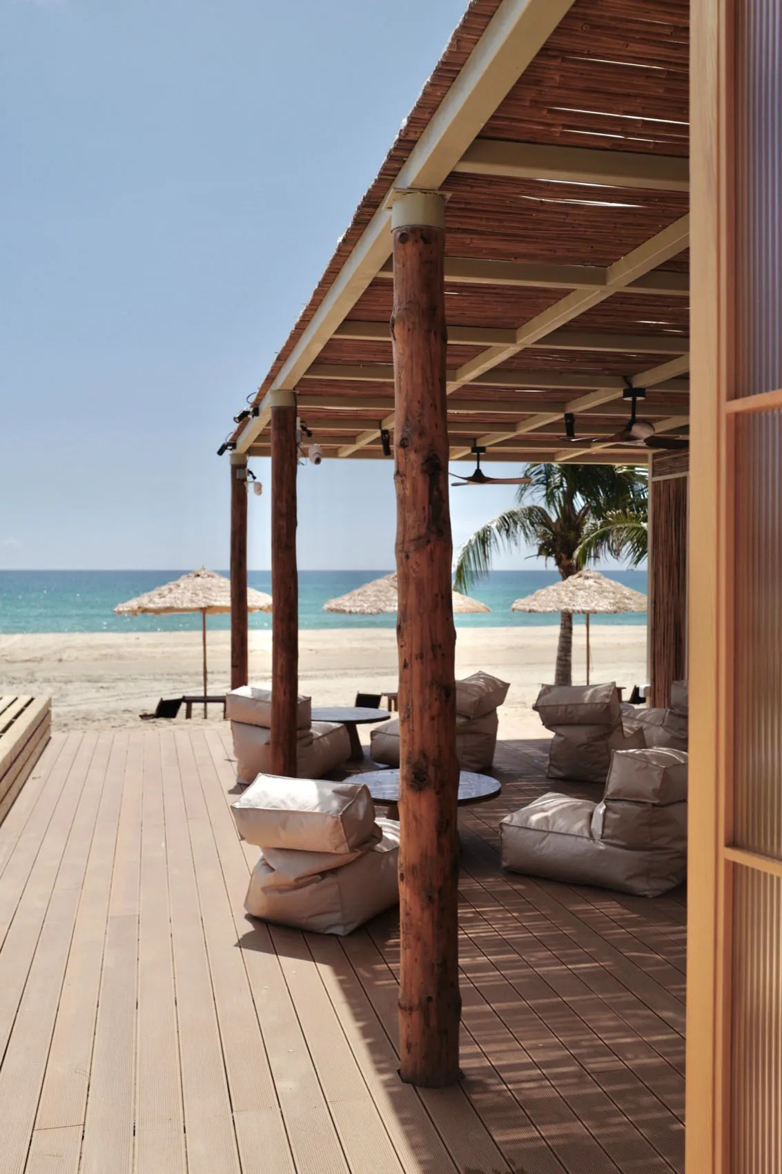 A beach house with a wooden deck overlooking the ocean, featuring chairs and umbrellas for a comfortable seating area