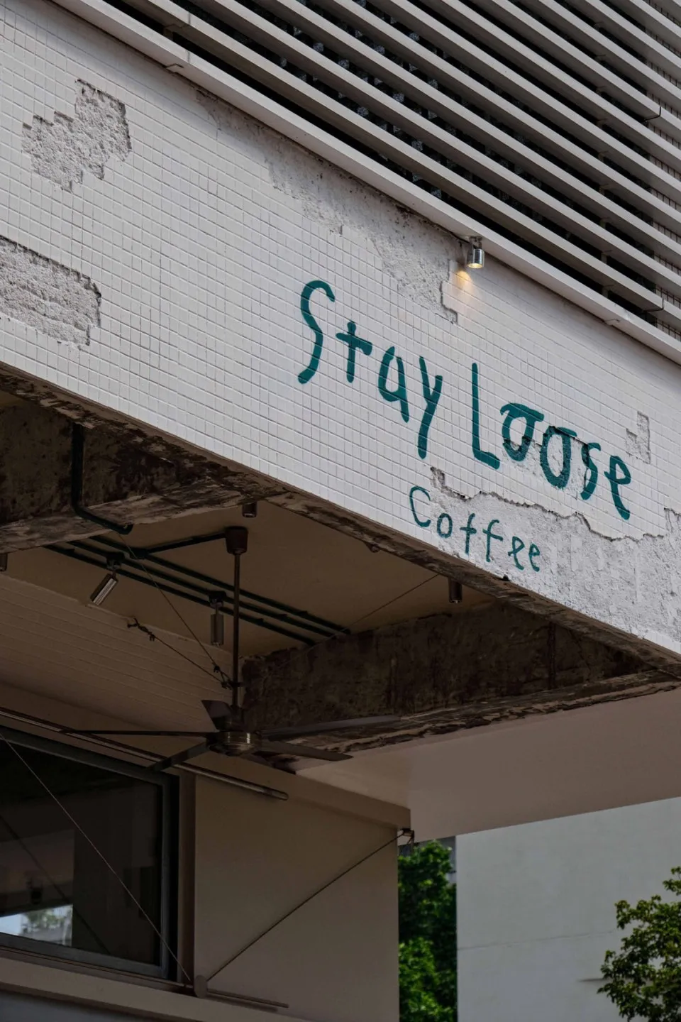 A cozy coffee shop with a white concrete exterior, a green sign reading Stay Loose Coffee, and a welcoming atmosphere