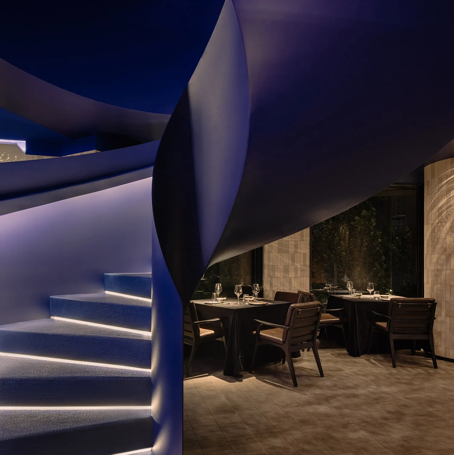 Elegant restaurant interior with a spiral metal staircase, tables, chairs, and wine glasses, creating an upscale and inviting atmosphere