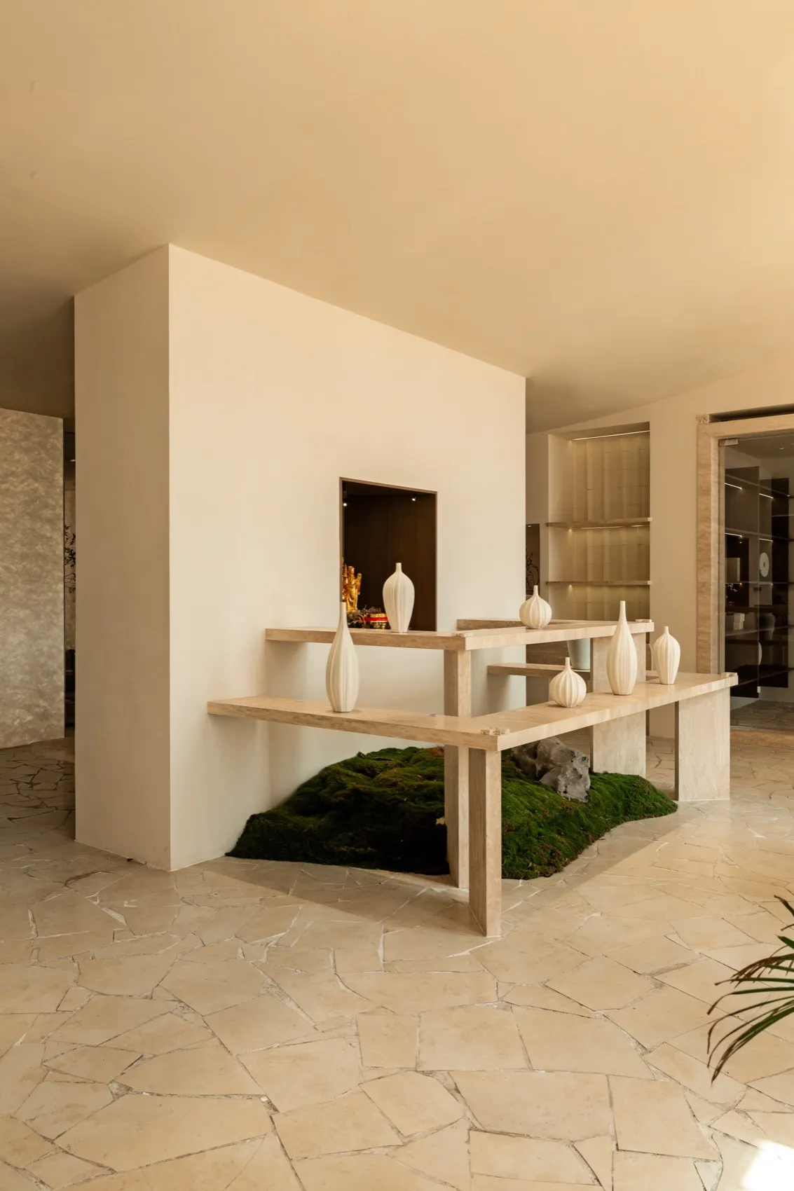 A minimalist interior design showroom featuring a table with six vases of various sizes and shapes, set against a clean white wall