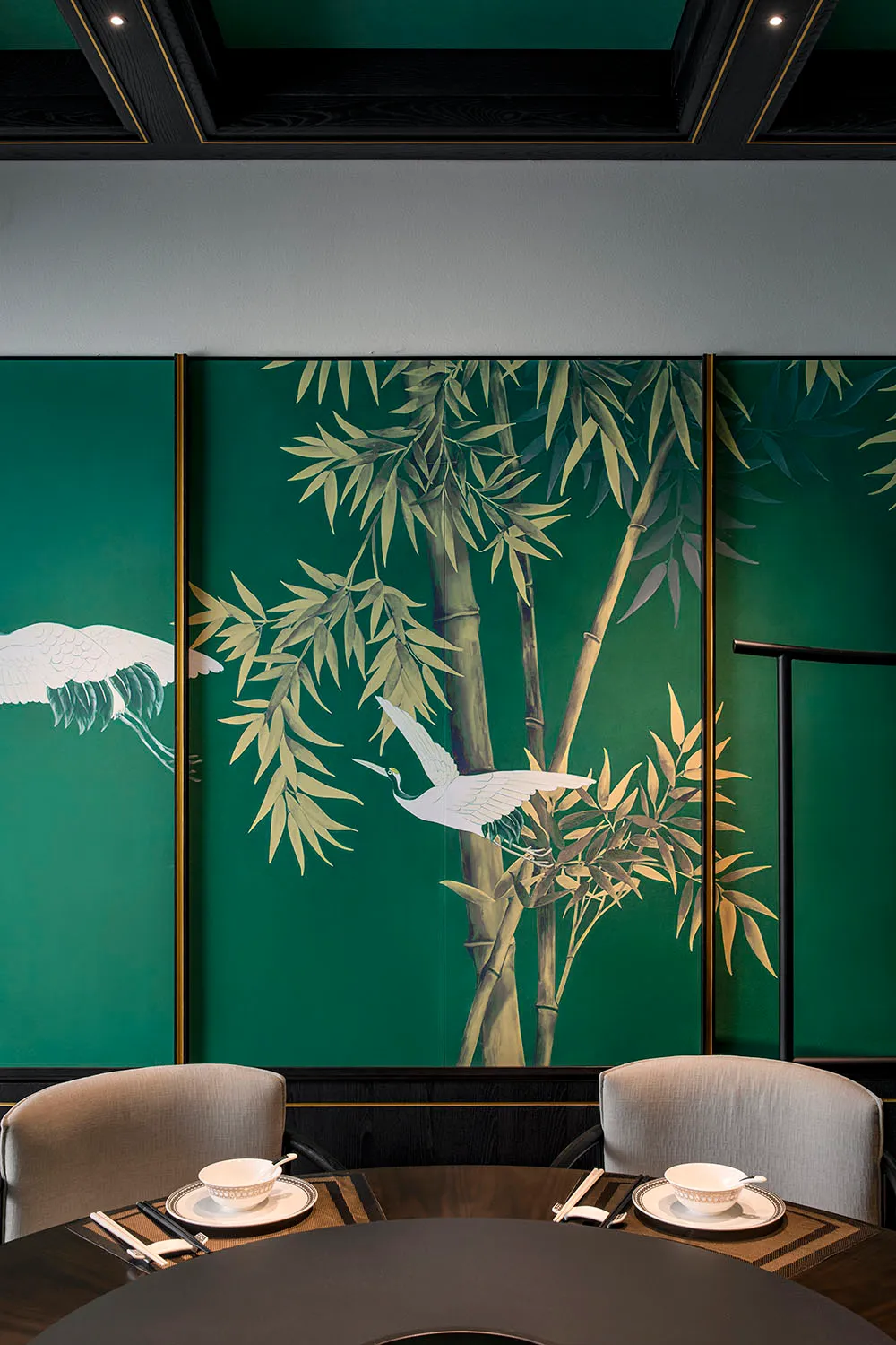 Serene living space with green walls, artwork of birds on bamboo trees, and two chairs in a calming environment