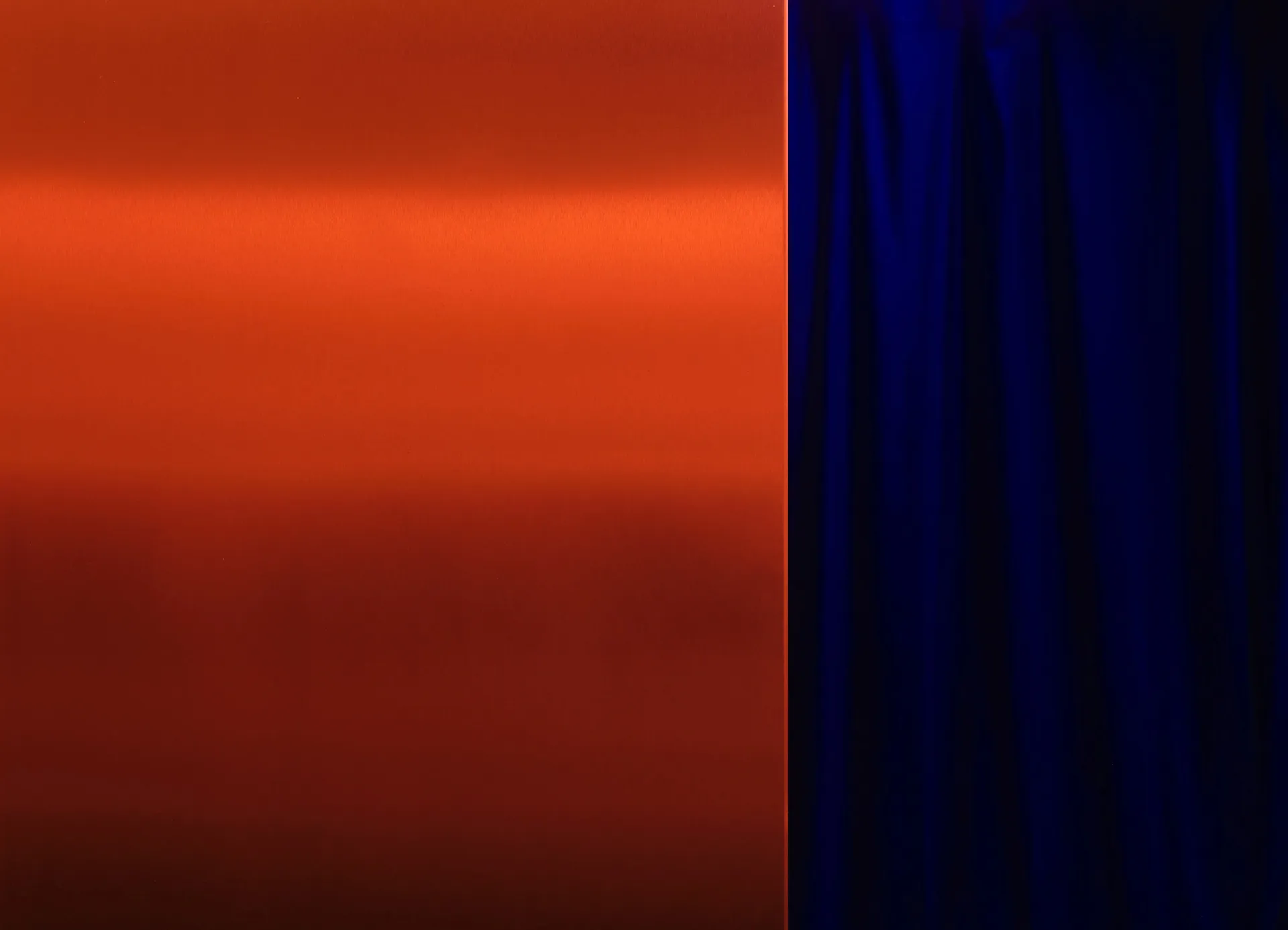 A modern interior space with an orange metal wall and a blue curtain, creating a striking contrast between the two colors