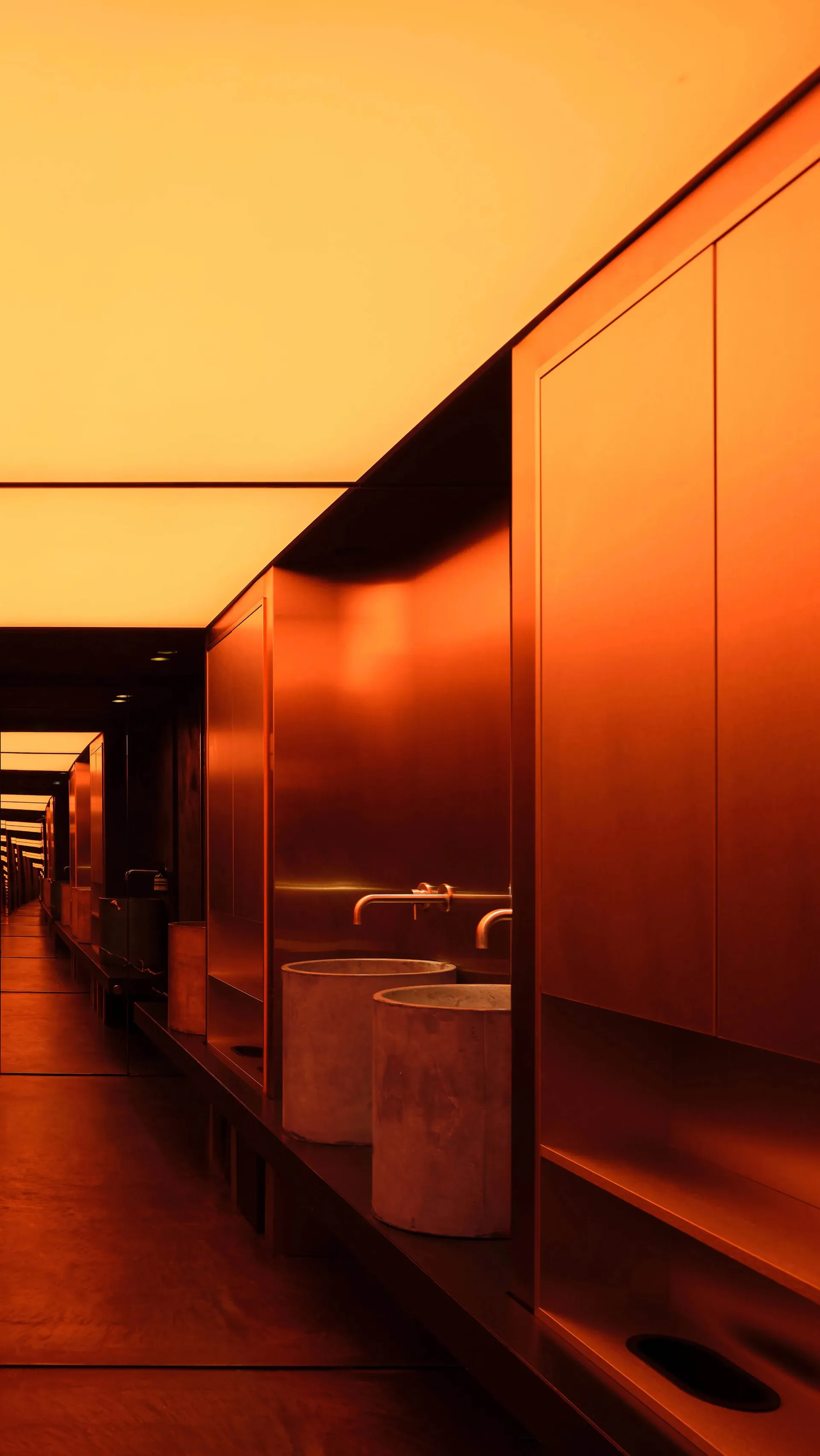 A hotel corridor with orange walls, two sinks, mirrors, and trash cans, suggesting a clean and well-maintained environment