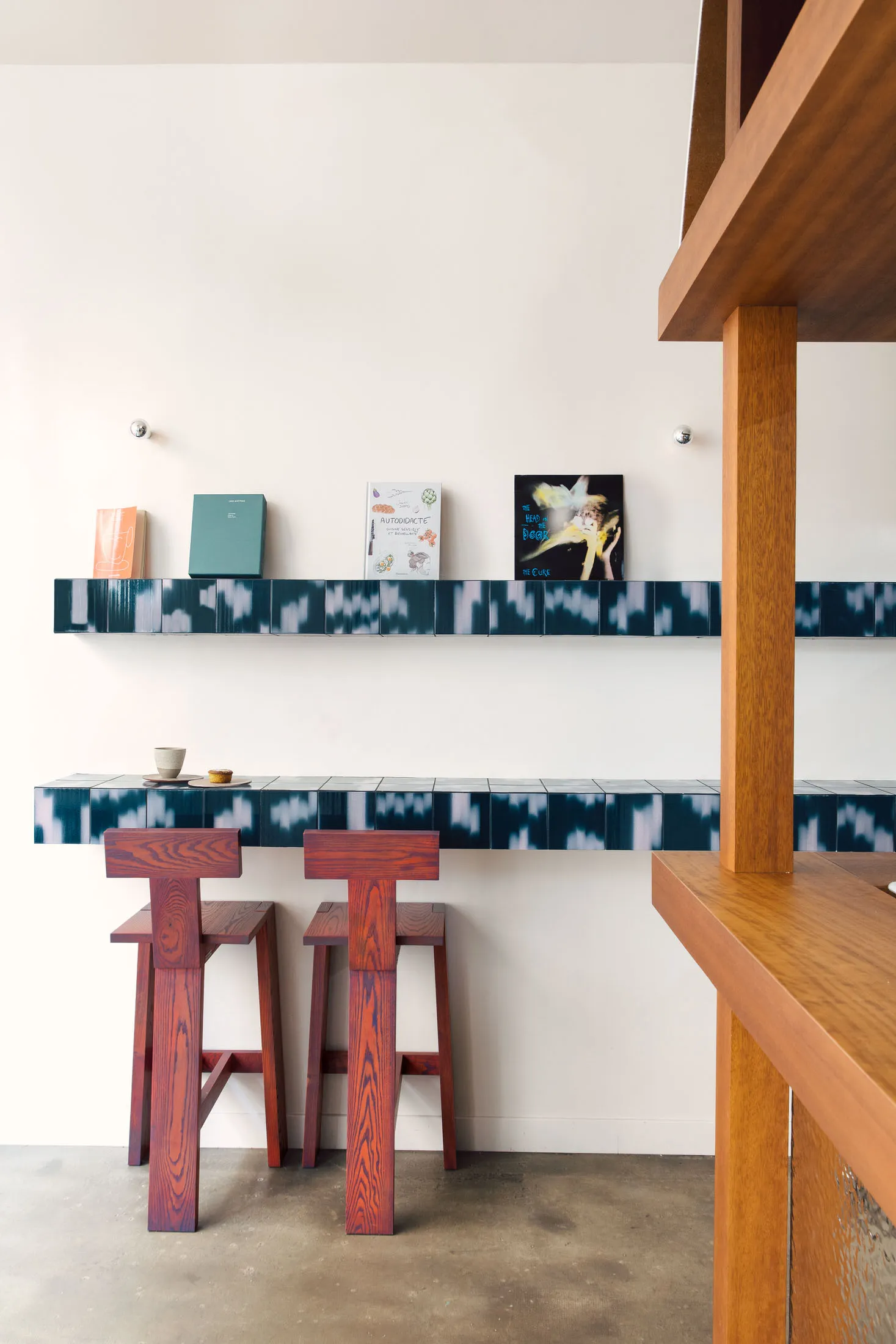 Modern kitchen with wooden elements, black and white tiles, and casual seating area with stools and scattered books