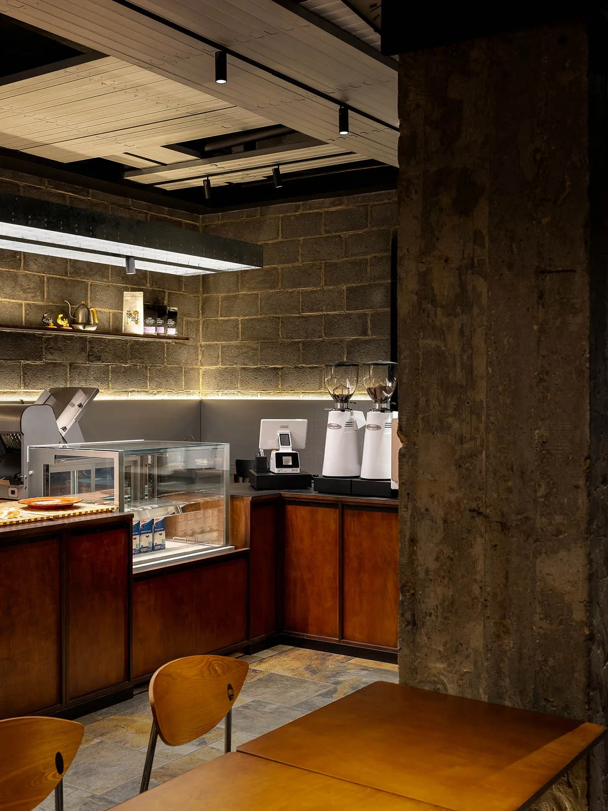 Cozy cafe interior with brick walls, wooden elements, and a dining table, featuring a counter with various items and appliances