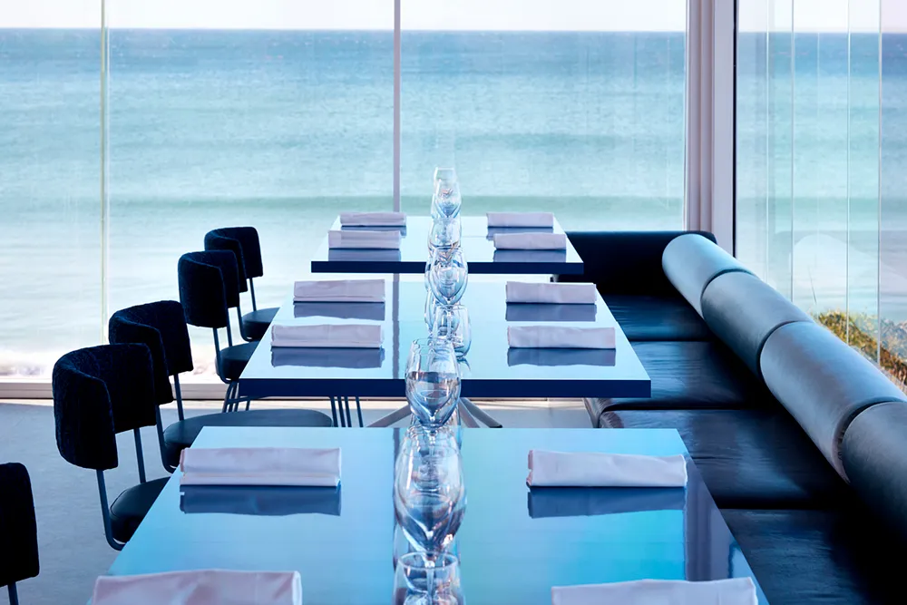 Elegant oceanfront dining room with a large table set for a meal, surrounded by chairs and overlooking the ocean