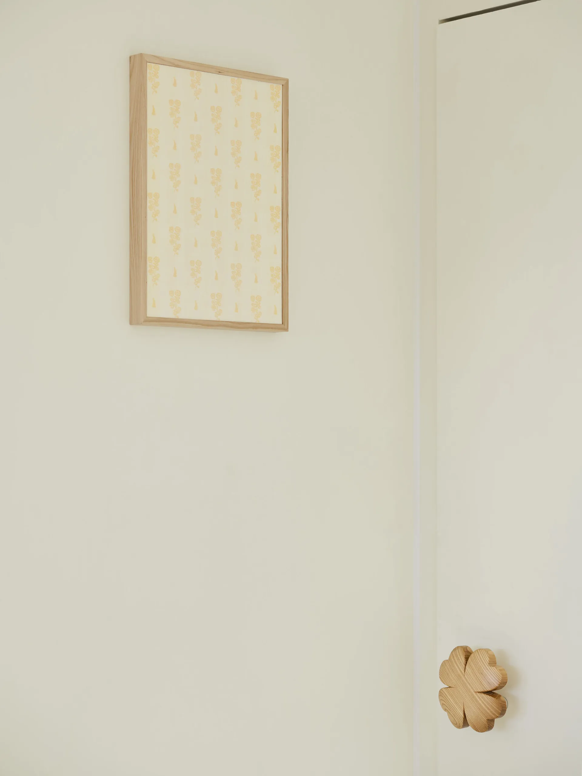 A clean and minimalistic room with a white wall featuring two framed pictures, one with a yellow background and the other with a brown frame, and two wooden decorative elements at the bottom