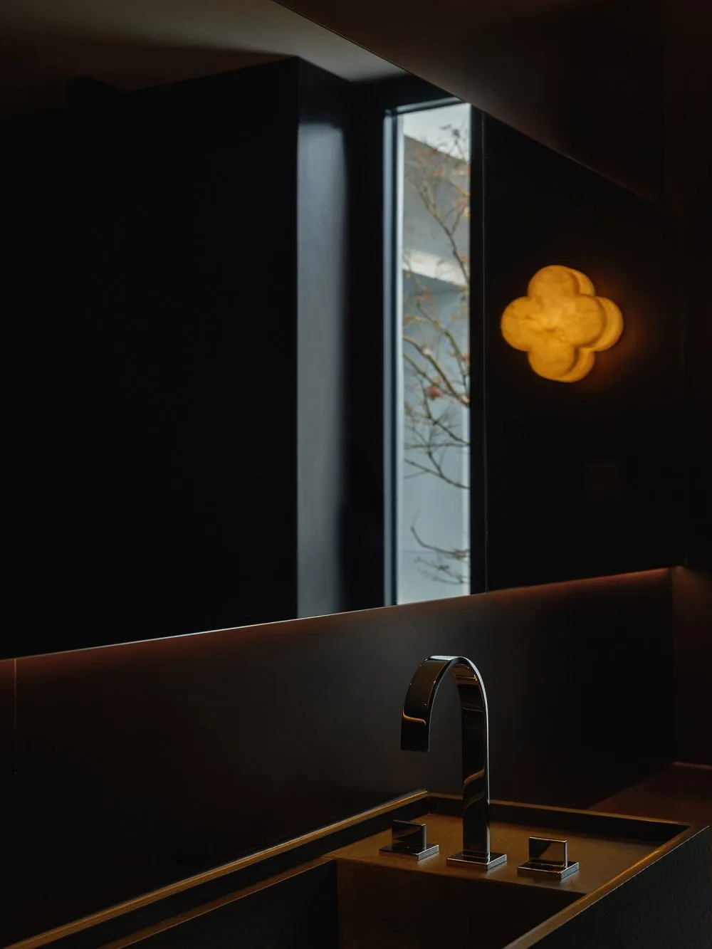 Modern bathroom with a metal sink, black walls, and two windows, giving off an elegant and minimalist vibe