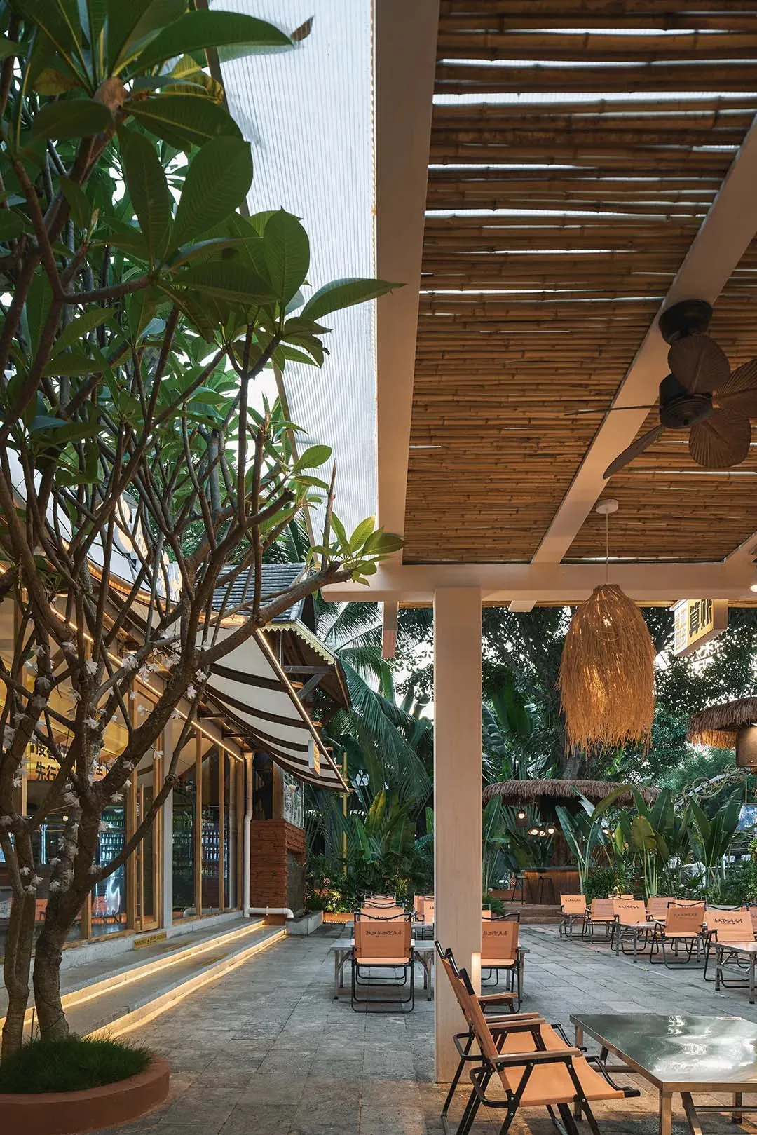 Outdoor dining area with a thatched roof, palm trees, and comfortable seating with cushions