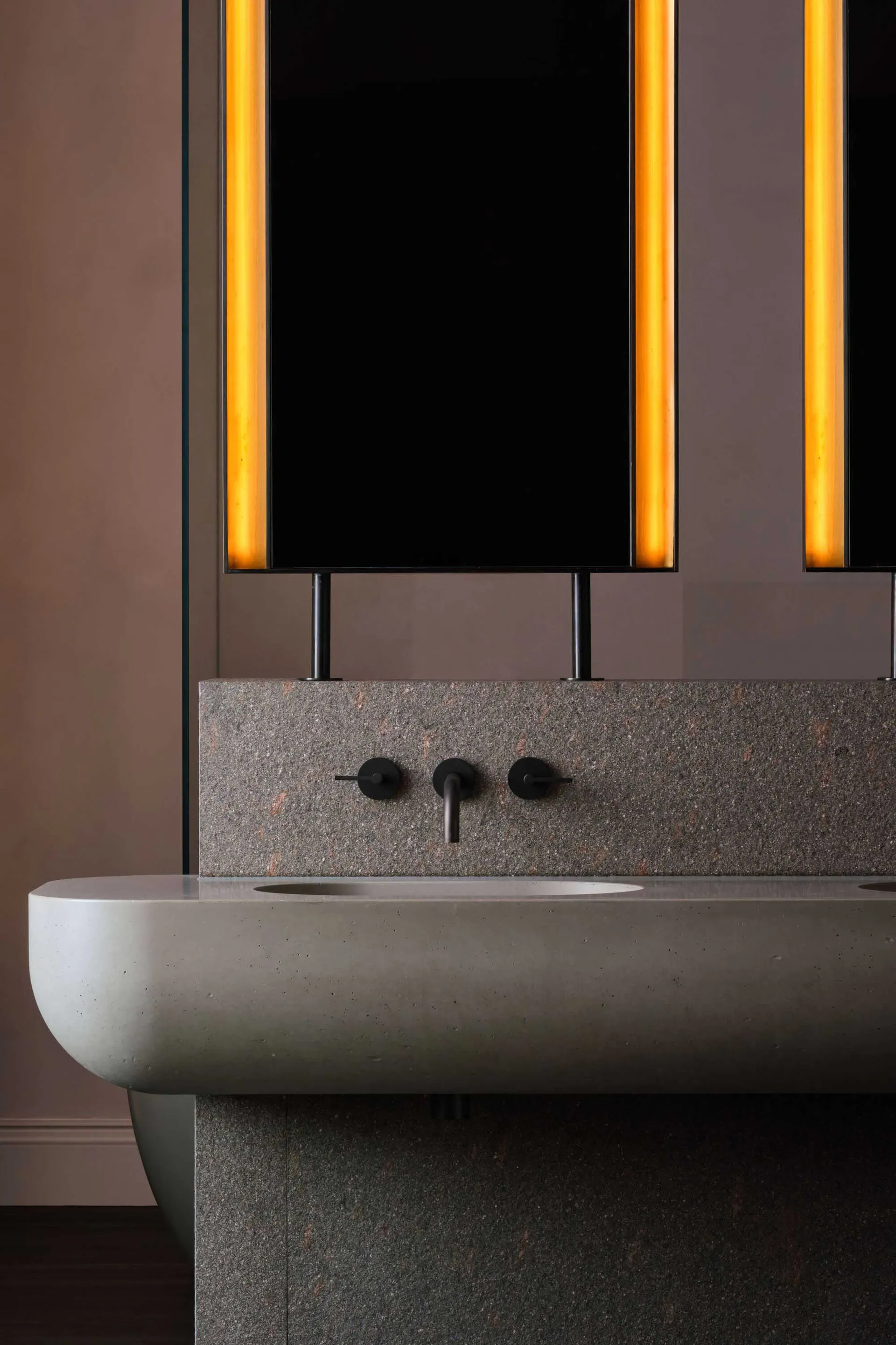 A bathroom with two sinks, marble countertops, and an orange glow creating a warm atmosphere
