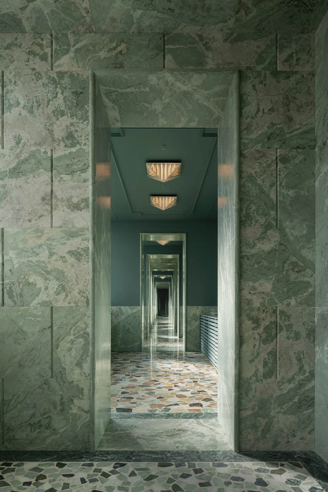 Elegant hallway with marble walls and floor, symmetrical doors, and overhead lighting