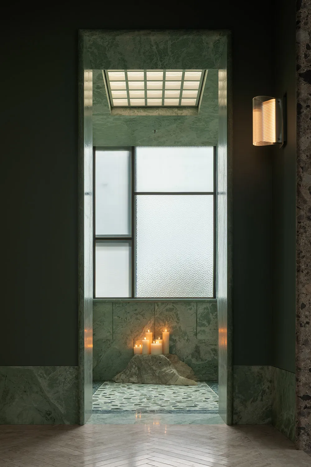 Bathroom with a green tiled wall, a shower area, and lit candles creating a warm and relaxing atmosphere
