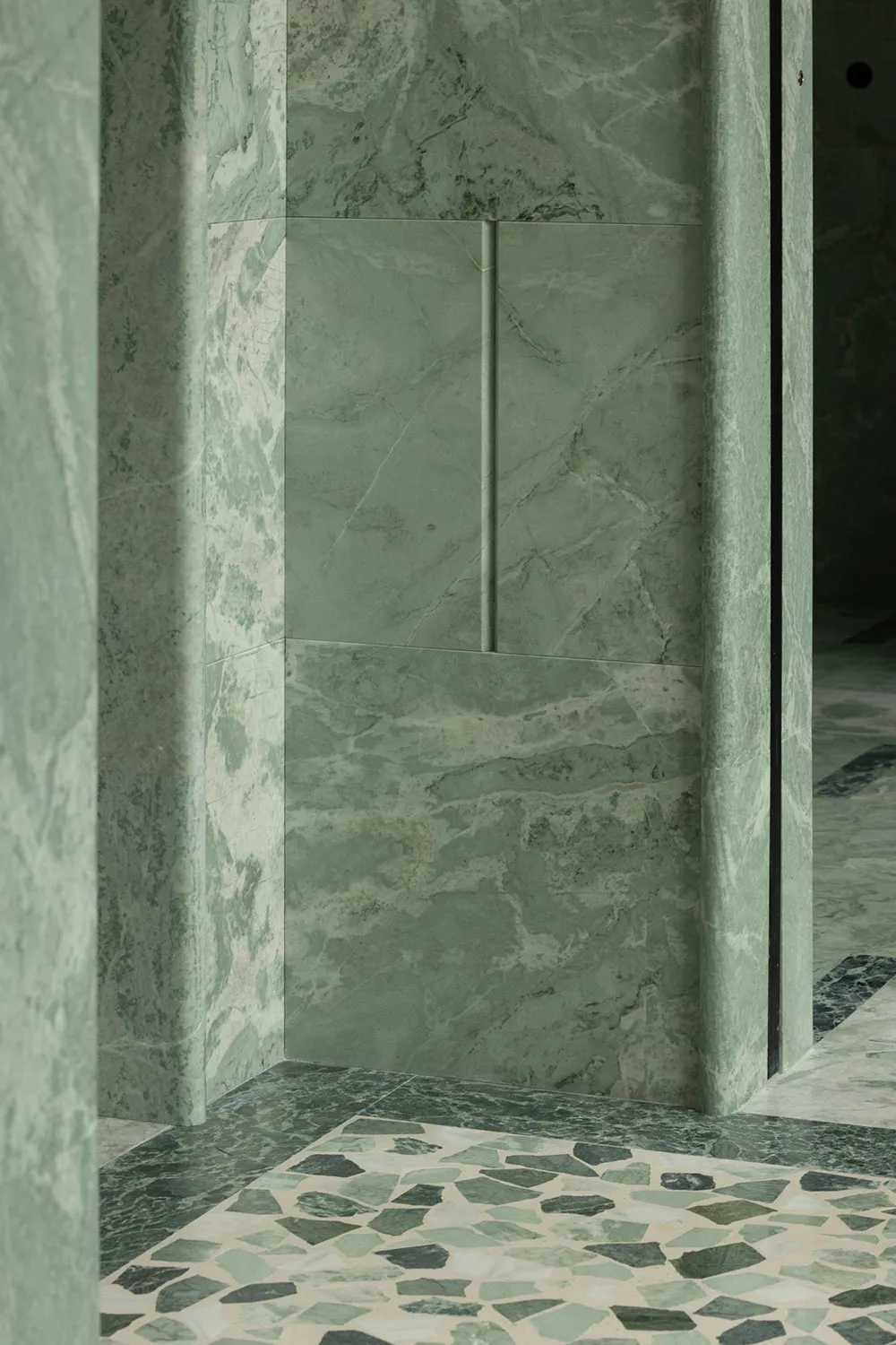 Bathroom with a green-tinted marble wall, two doors, and a sink, showcasing a well-designed space with a distinctive feature
