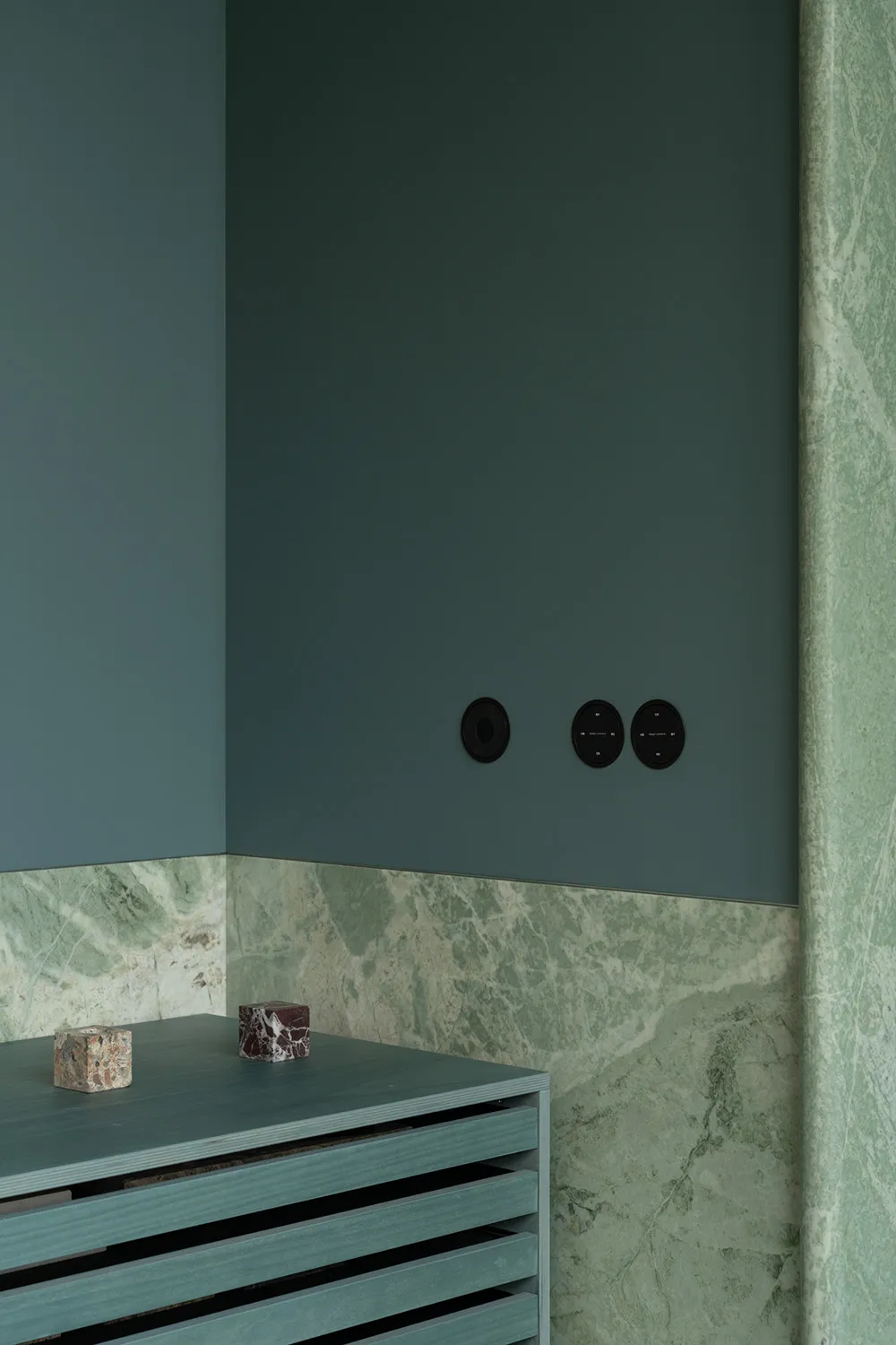 A large, well-lit room with a green wall, marble countertop, and two clocks on the wall, creating a calm and inviting atmosphere