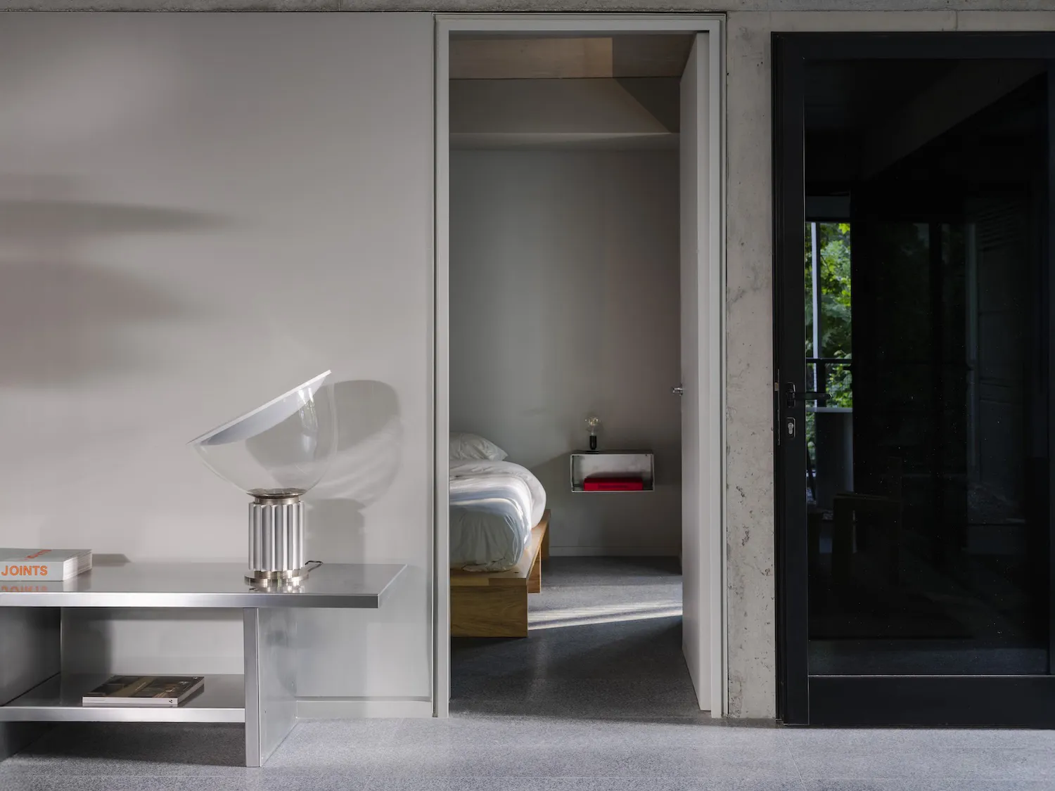 A calm bedroom with two beds and a chair, featuring a double bed near the door and a smaller bed further back, with a chair nearby