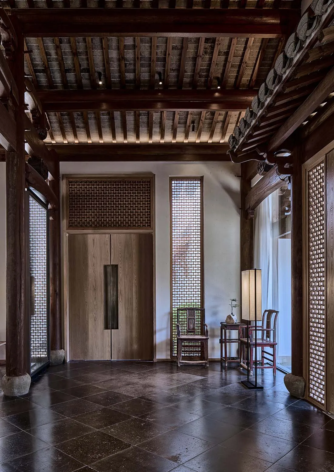 Asian-style interior design with wooden floors and walls, featuring a large wooden door, two chairs, and a vase on a surface near the right wall, creating a calm and inviting atmosphere