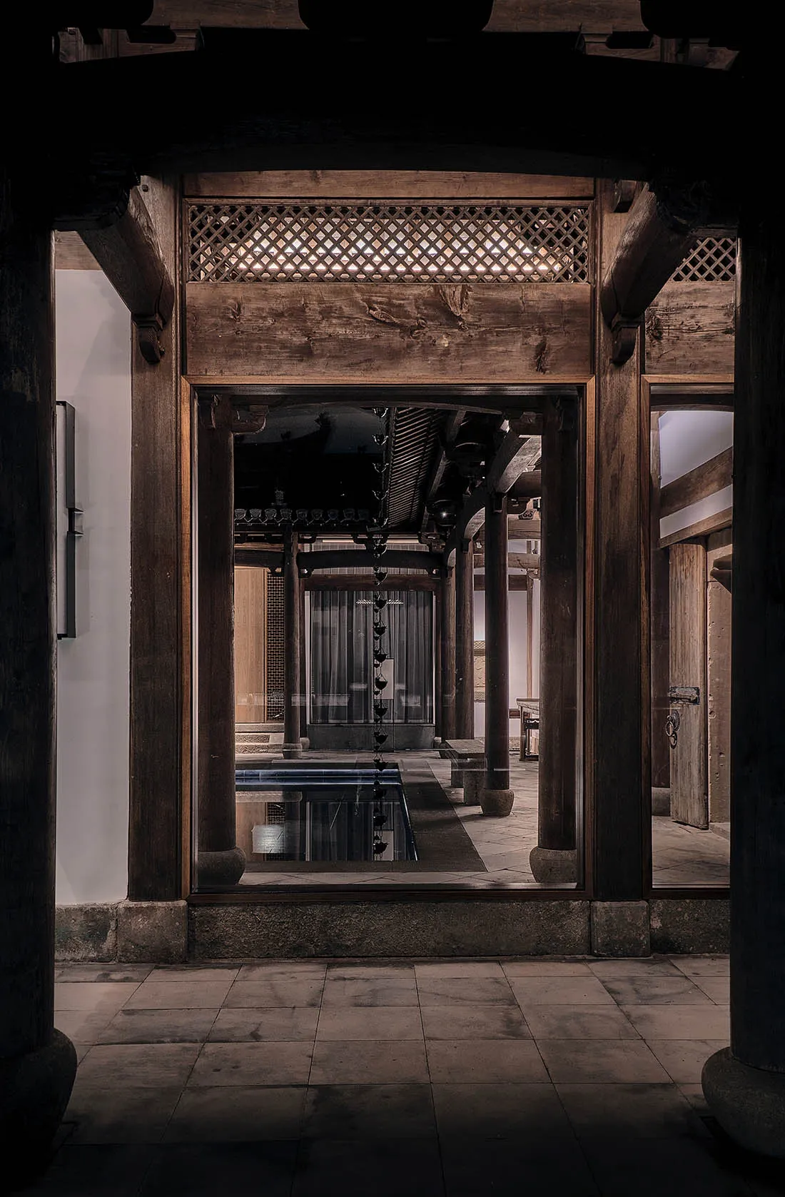 Traditional Asian building with wooden pillars and a stone archway, featuring multiple rooms with a pool and dining area
