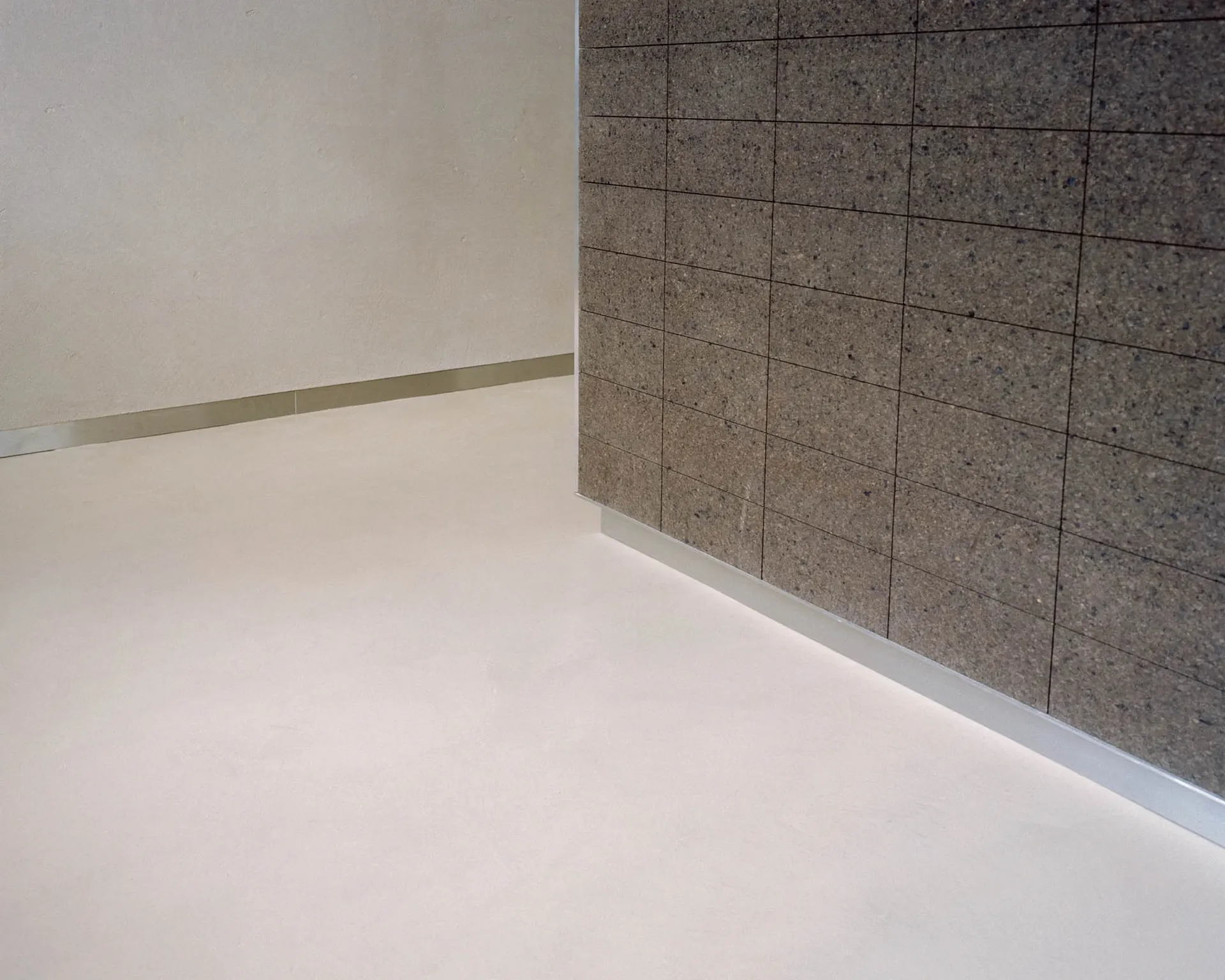A clean and well-lit hallway with a white tile floor, a mirror on one wall, and a doorway leading to another room