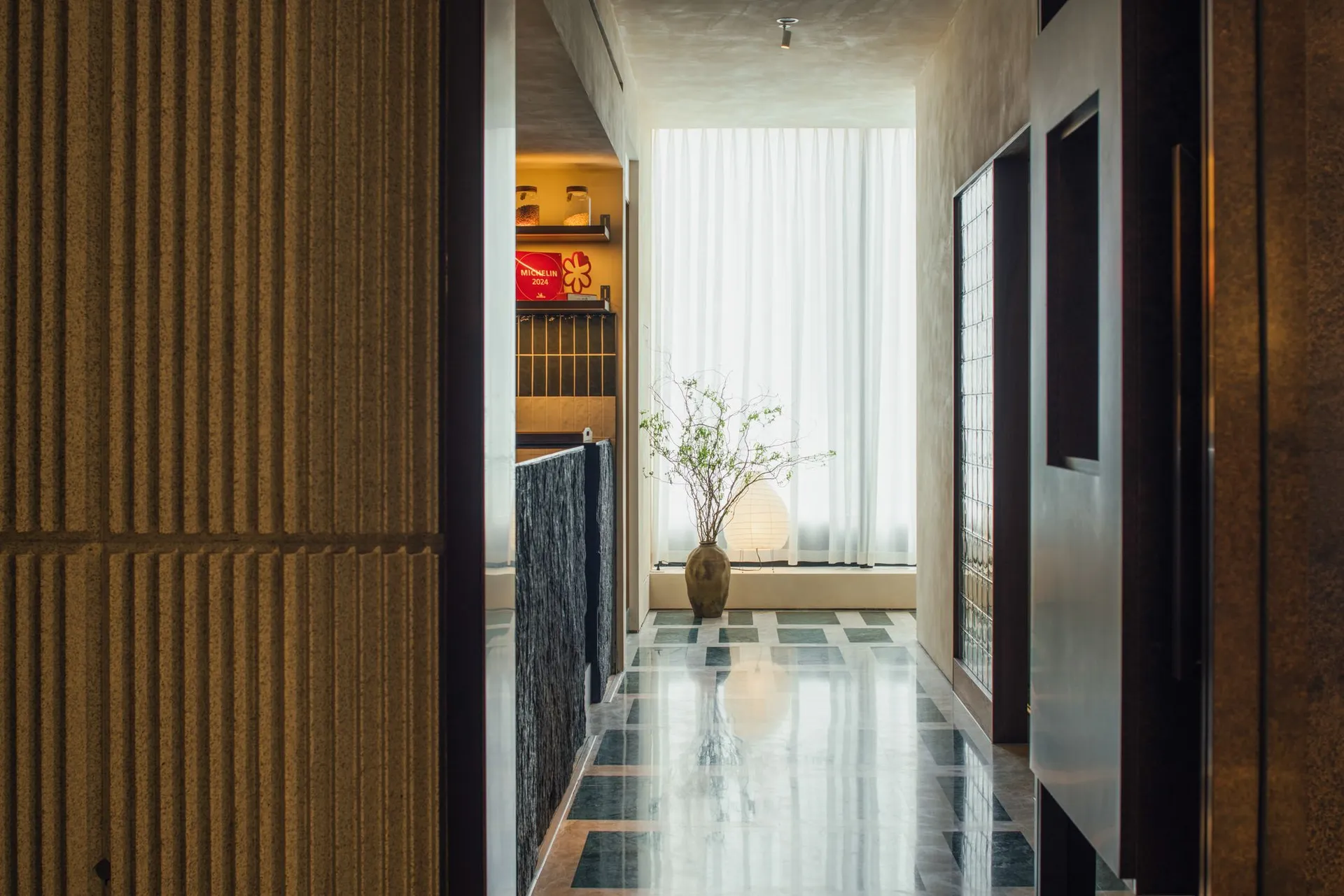A calm and organized hallway with a black and white color scheme, featuring a tiled floor and two potted plants