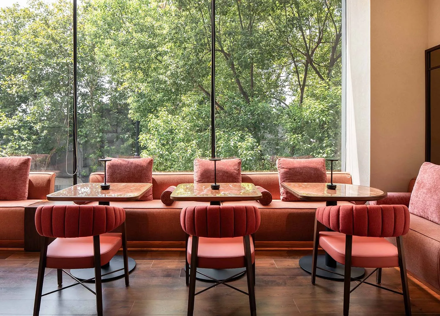 Dining area with multiple tables, chairs, and a bench, set against a backdrop of wooden floors and warm brown and white walls, bathed in natural light