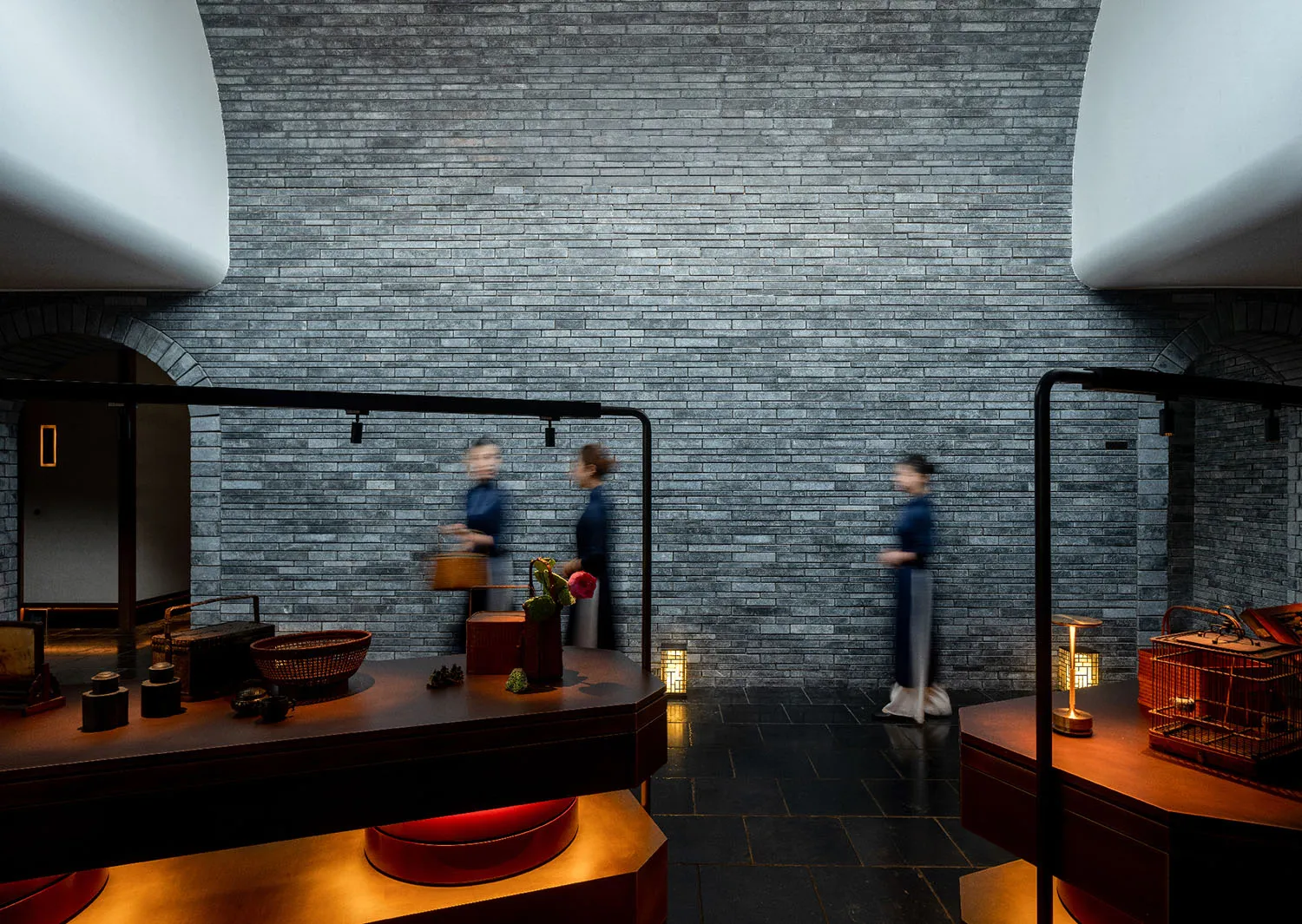 Three women walk through a traditional Chinese interior space with brick walls, potted plants, and decorative vases