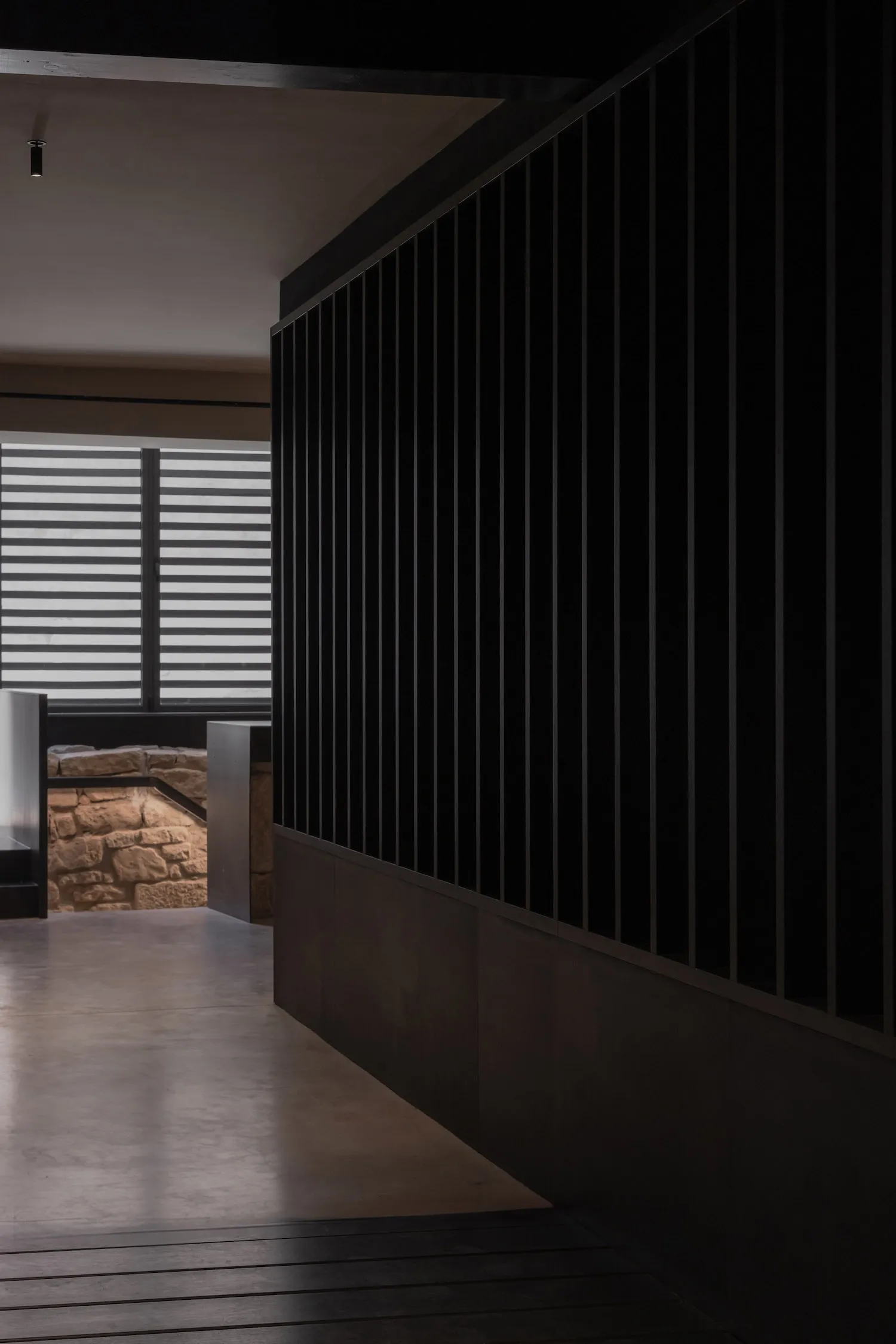 Dark room with black walls, a stone accent wall, and two windows on either side, lacking natural light