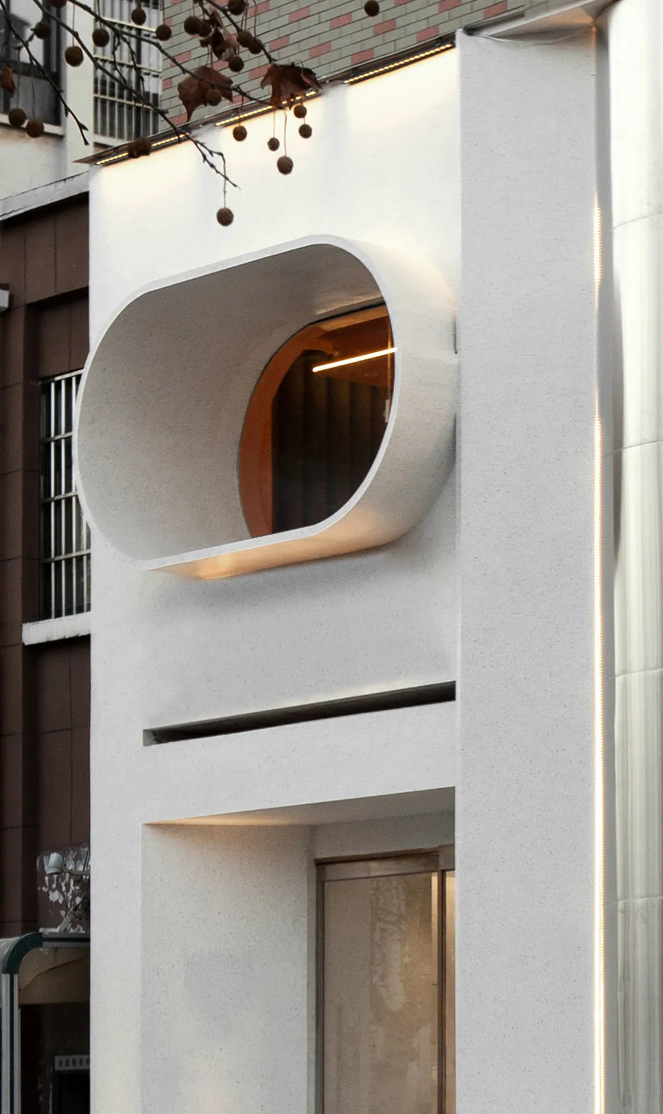 A modern building facade with a large white concrete wall featuring a round window, set against a neutral background