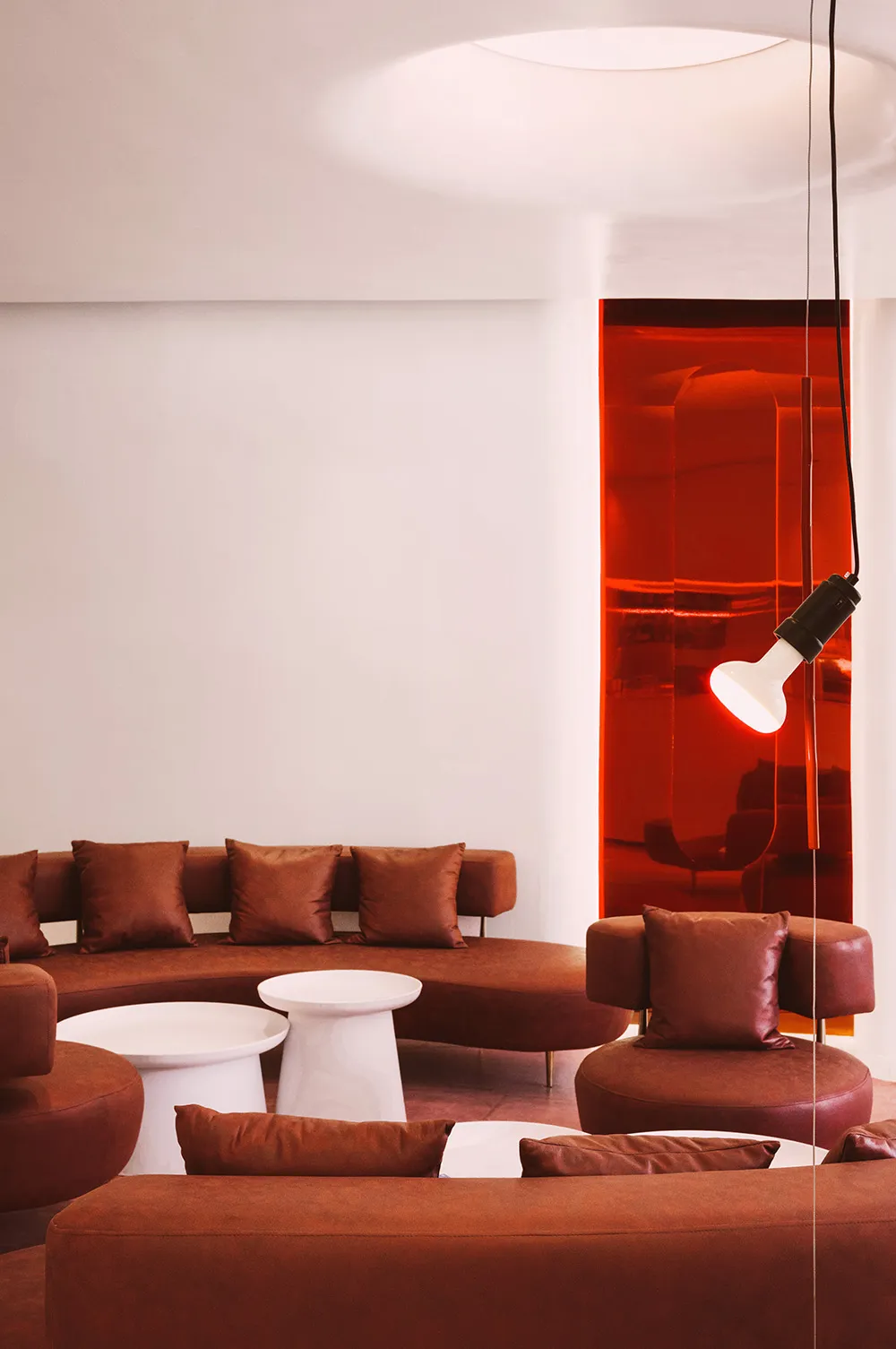 A modern living area with brown leather chairs and couches arranged around a coffee table, surrounded by red walls and white accents