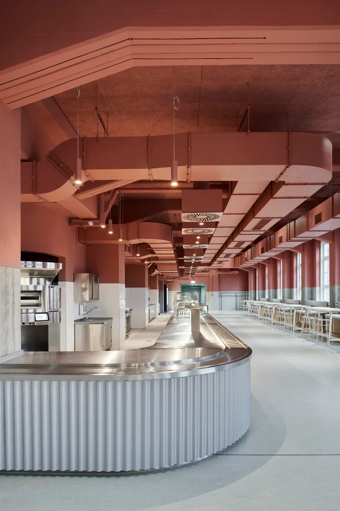 Industrial kitchen with a metal countertop island, various appliances, and chairs for staff to sit, with a clean and organized atmosphere