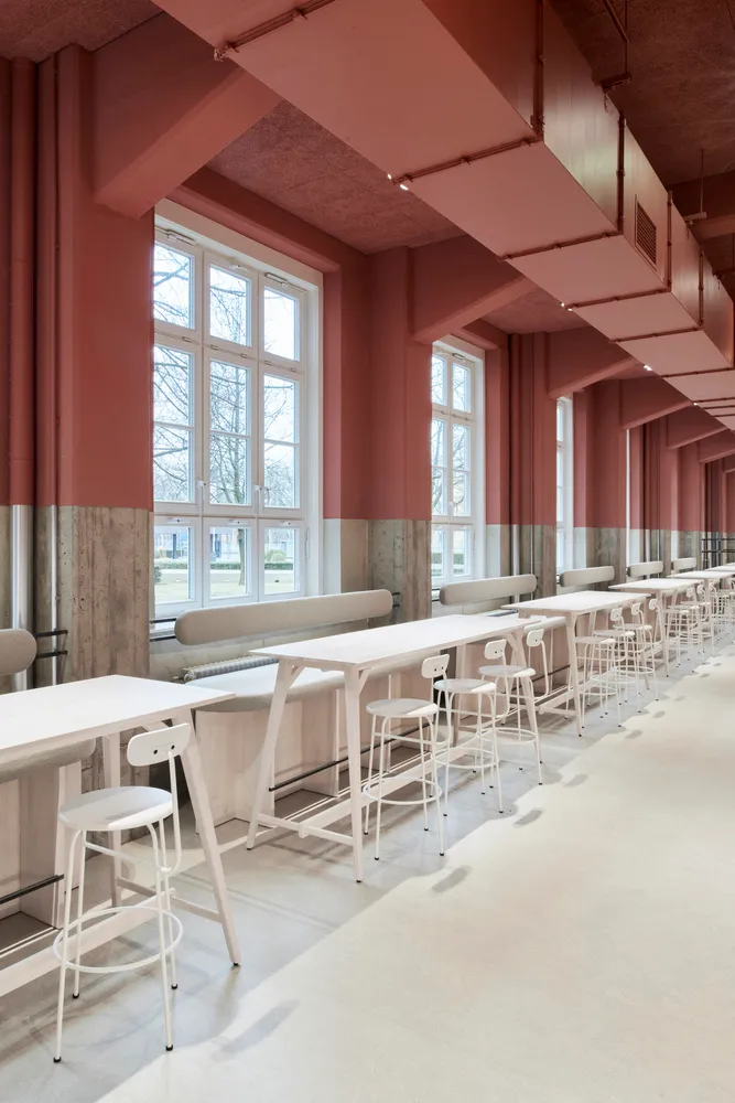 A modern dining space with pink walls, multiple tables, chairs, and benches, featuring a contemporary design with clean lines and minimalistic decoration