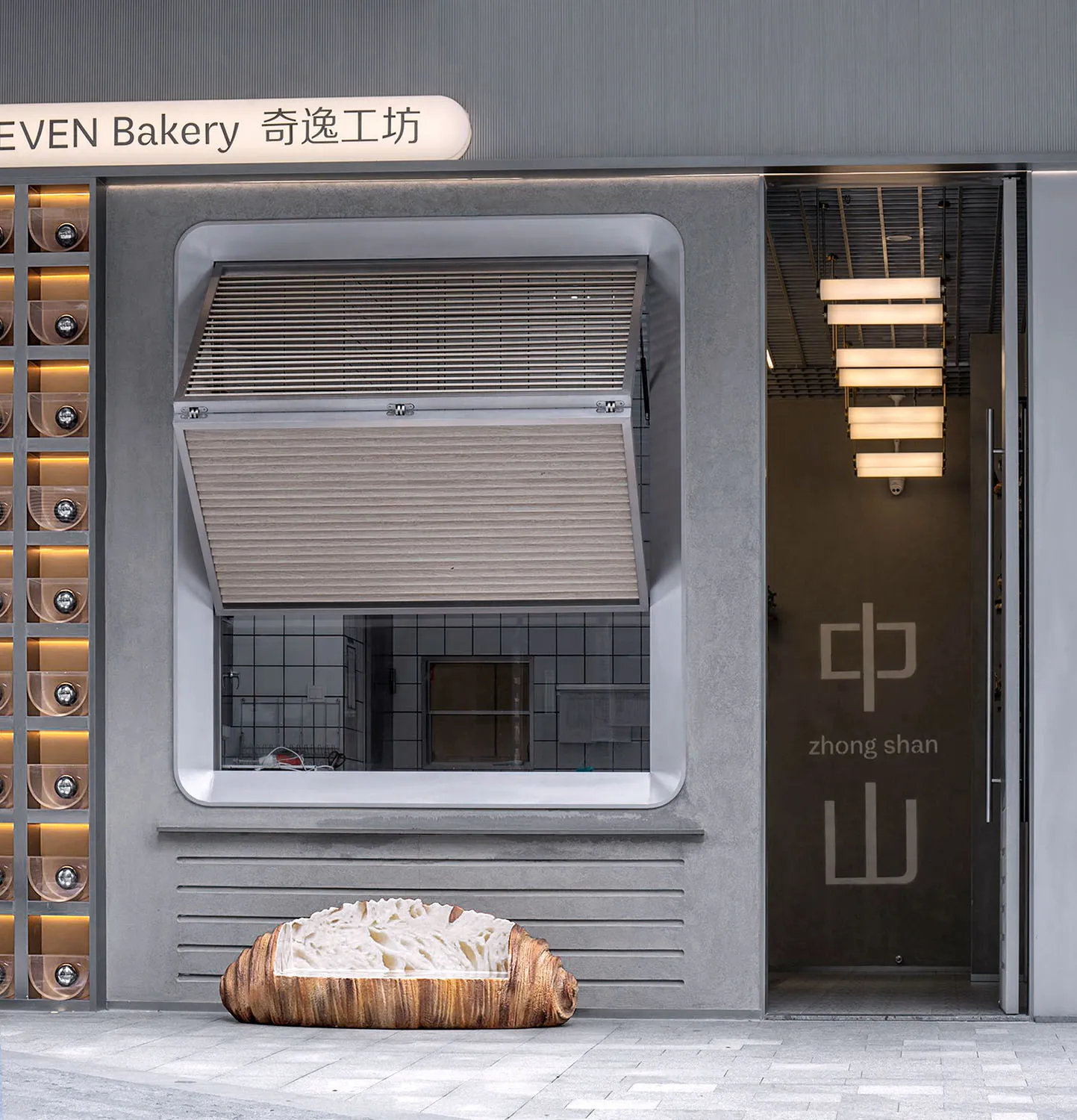 A modern Asian bakery storefront with a wooden sign, grey walls, and a glass front, displaying cakes and bowls with ingredients or decorations