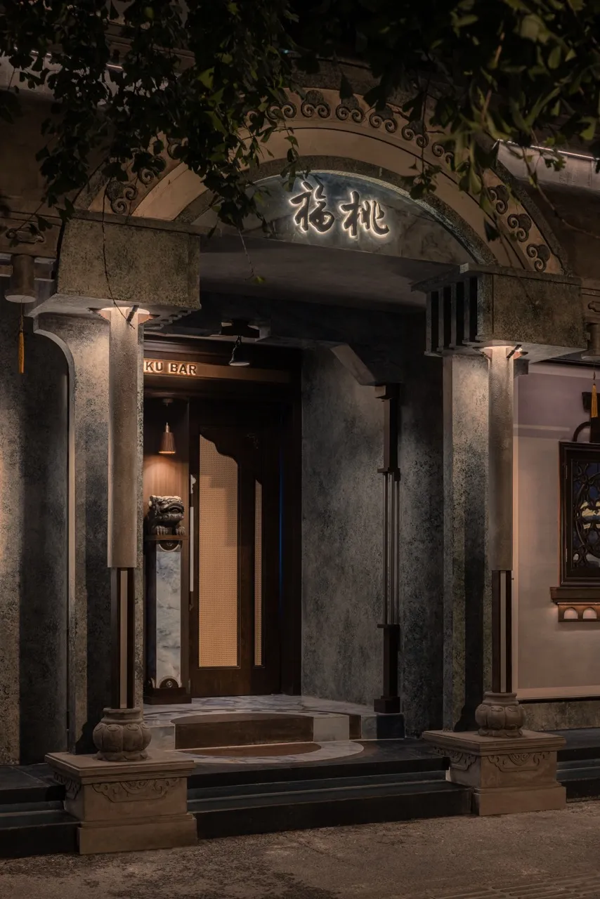 A warm and inviting restaurant entrance with a wooden doorway, stone construction, and soft lighting from two side lamps
