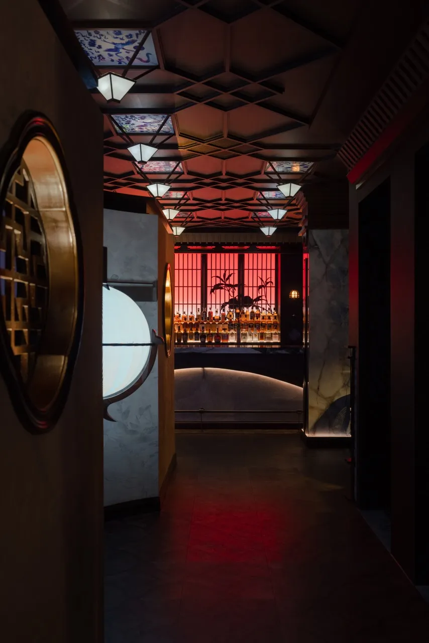 A sophisticated bar area with a long counter, bottles, wine glasses, and decorative elements, set against a dark background