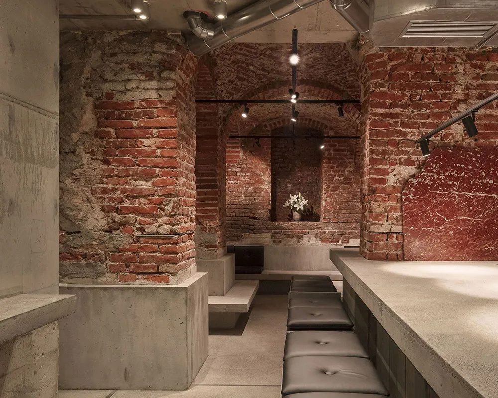 A large interior space with stone walls, brick floors, and several benches, giving off a vintage feel