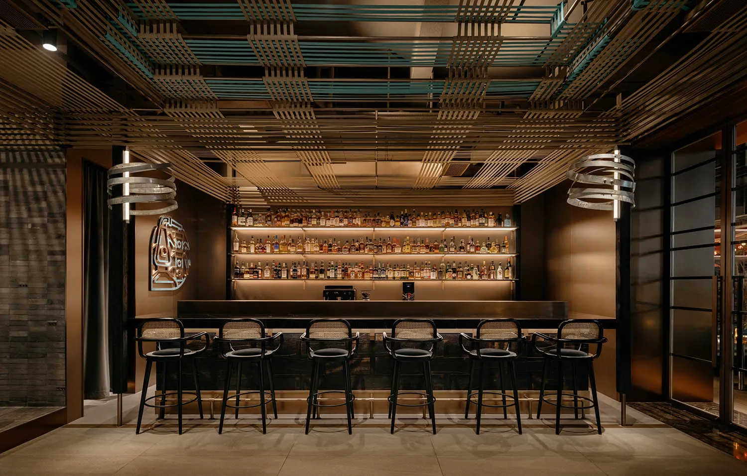 A modern bar with a long counter and stools, featuring bottles and a stylish design